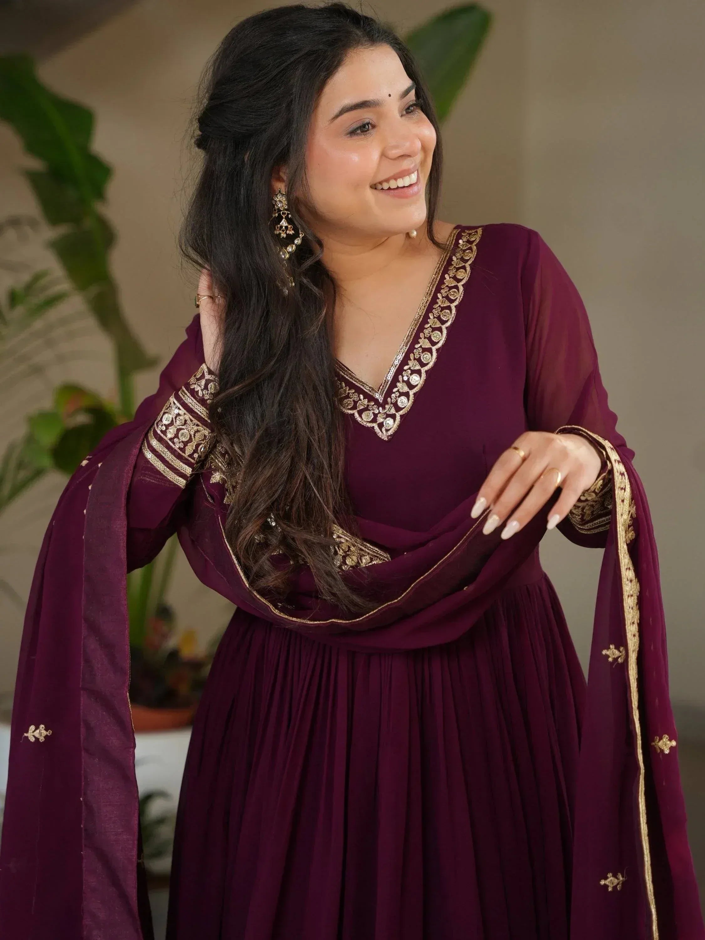 Woman in maroon ethnic gown with gold embroidery, perfect for Indian occasions and festive wear.