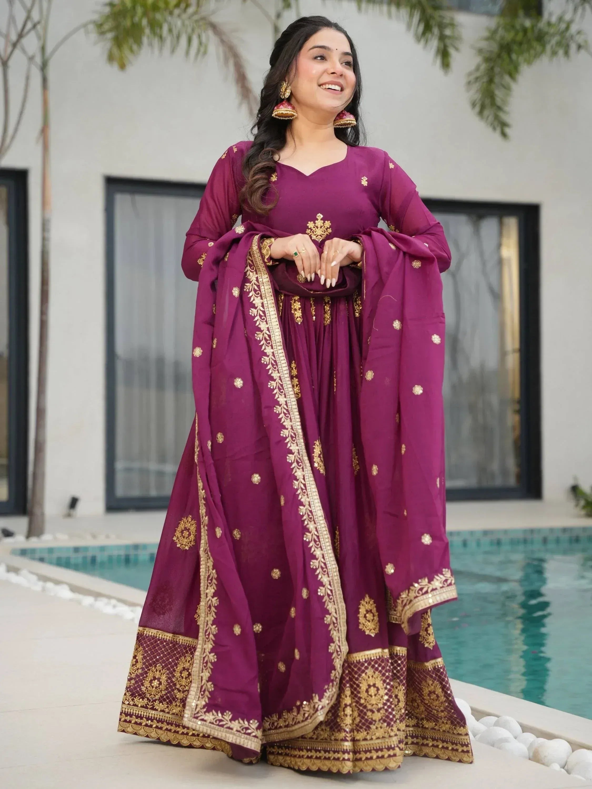 Woman in purple Indian ethnic wear with gold embroidery, standing by poolside, perfect for festive occasions.