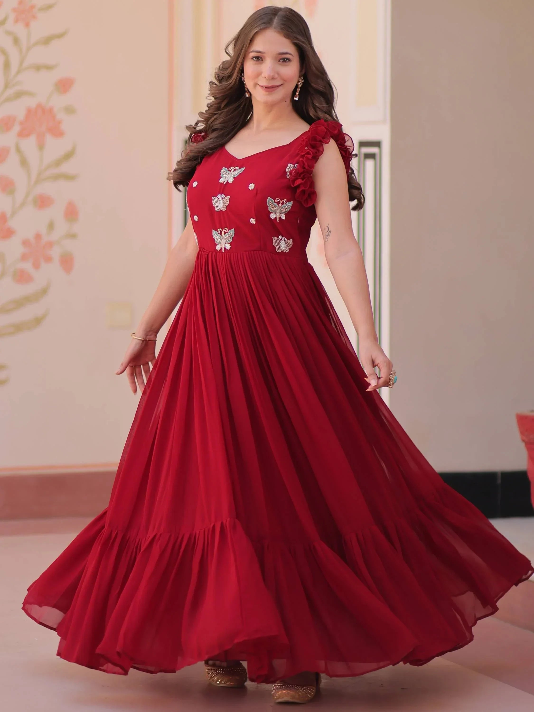 Woman in maroon ethnic gown with butterfly embroidery and ruffle sleeves, indoors