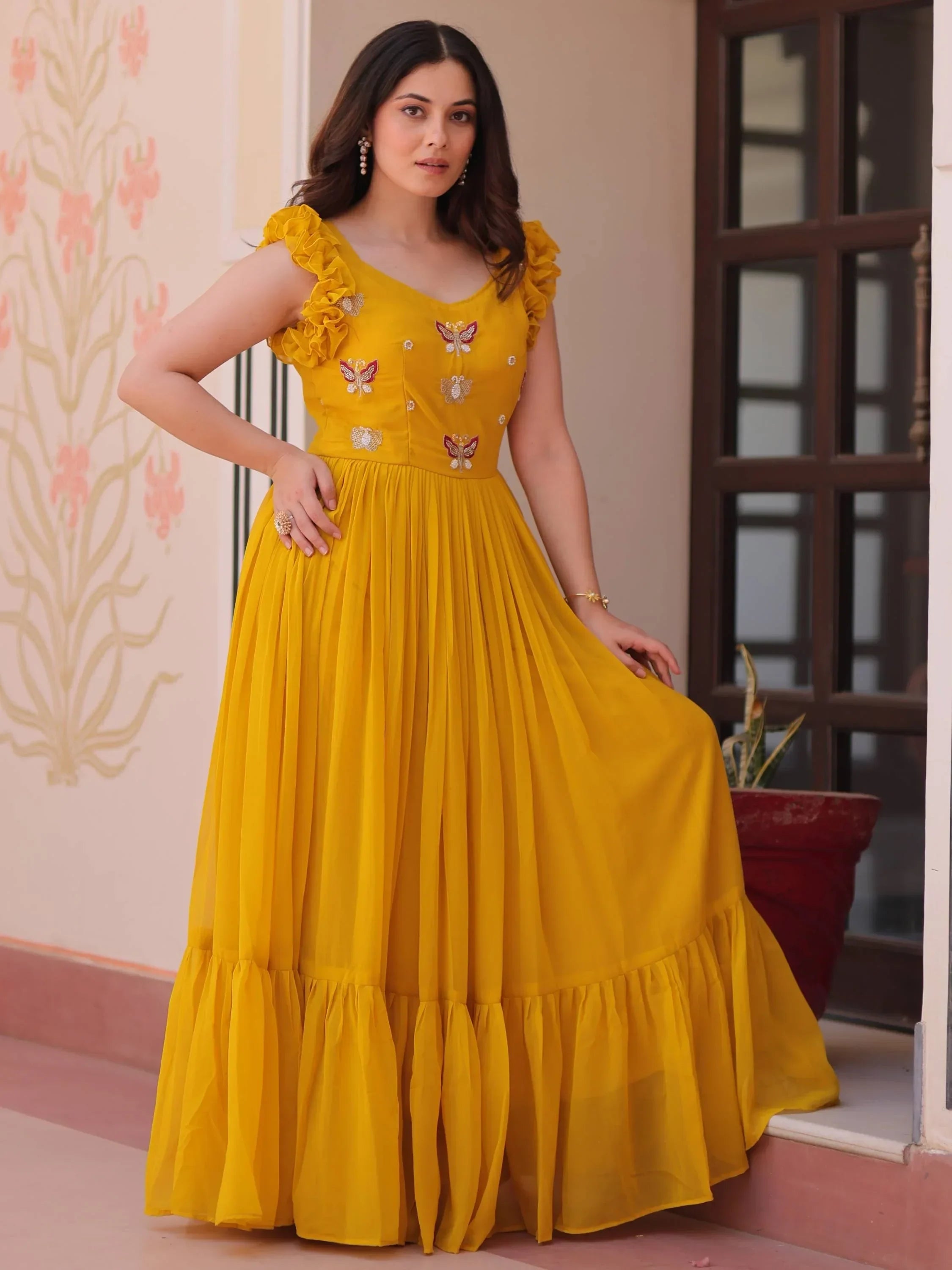 Woman in yellow ethnic gown with ruffled sleeves and floral embroidery, posing outdoors