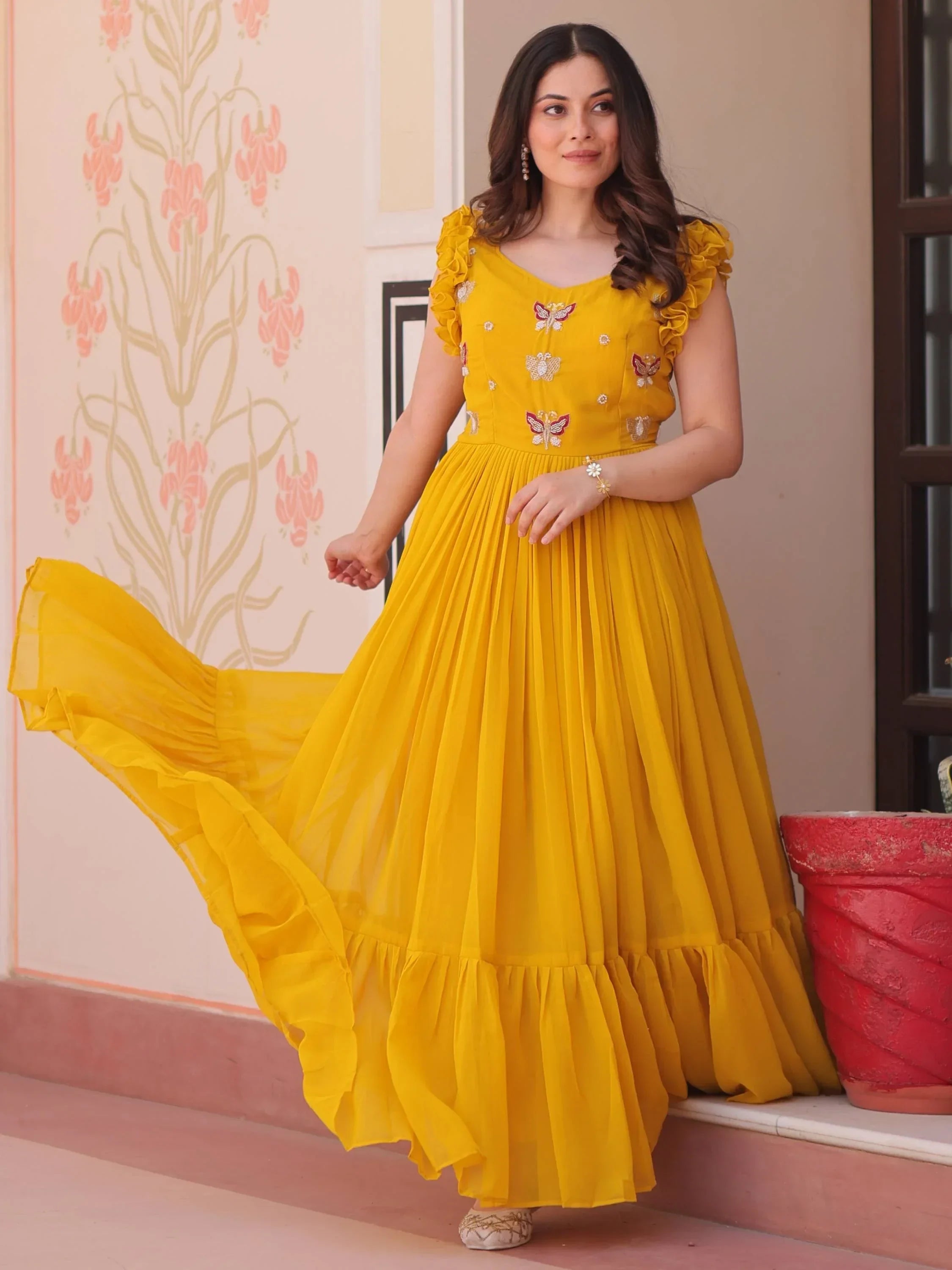 Woman in yellow embroidered ethnic gown with ruffled sleeves, flowing pleated skirt