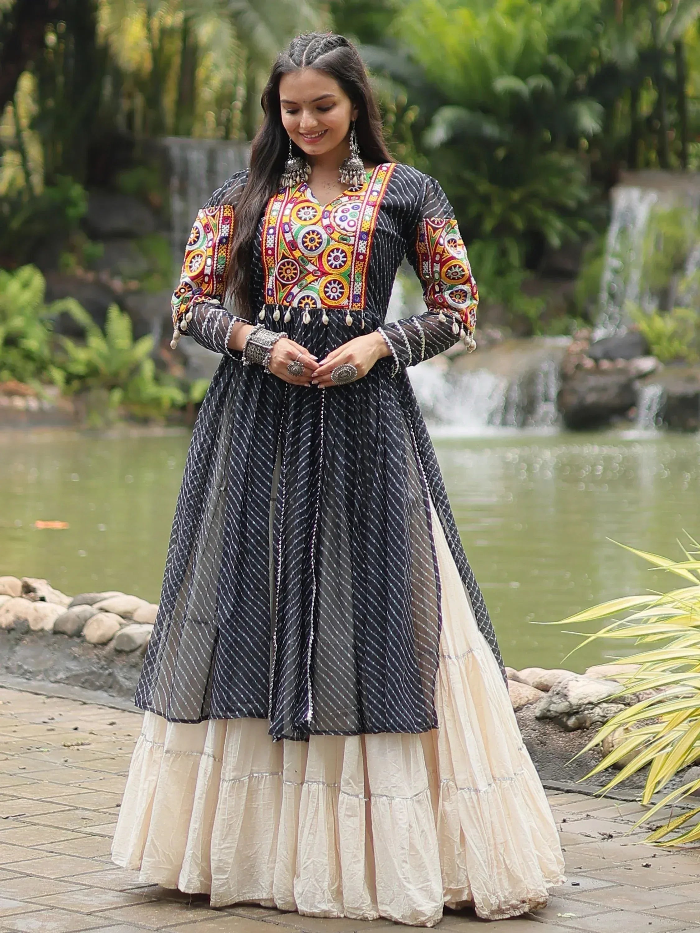 Black and cream ethnic anarkali with colorful mirror work, worn by woman near garden pond