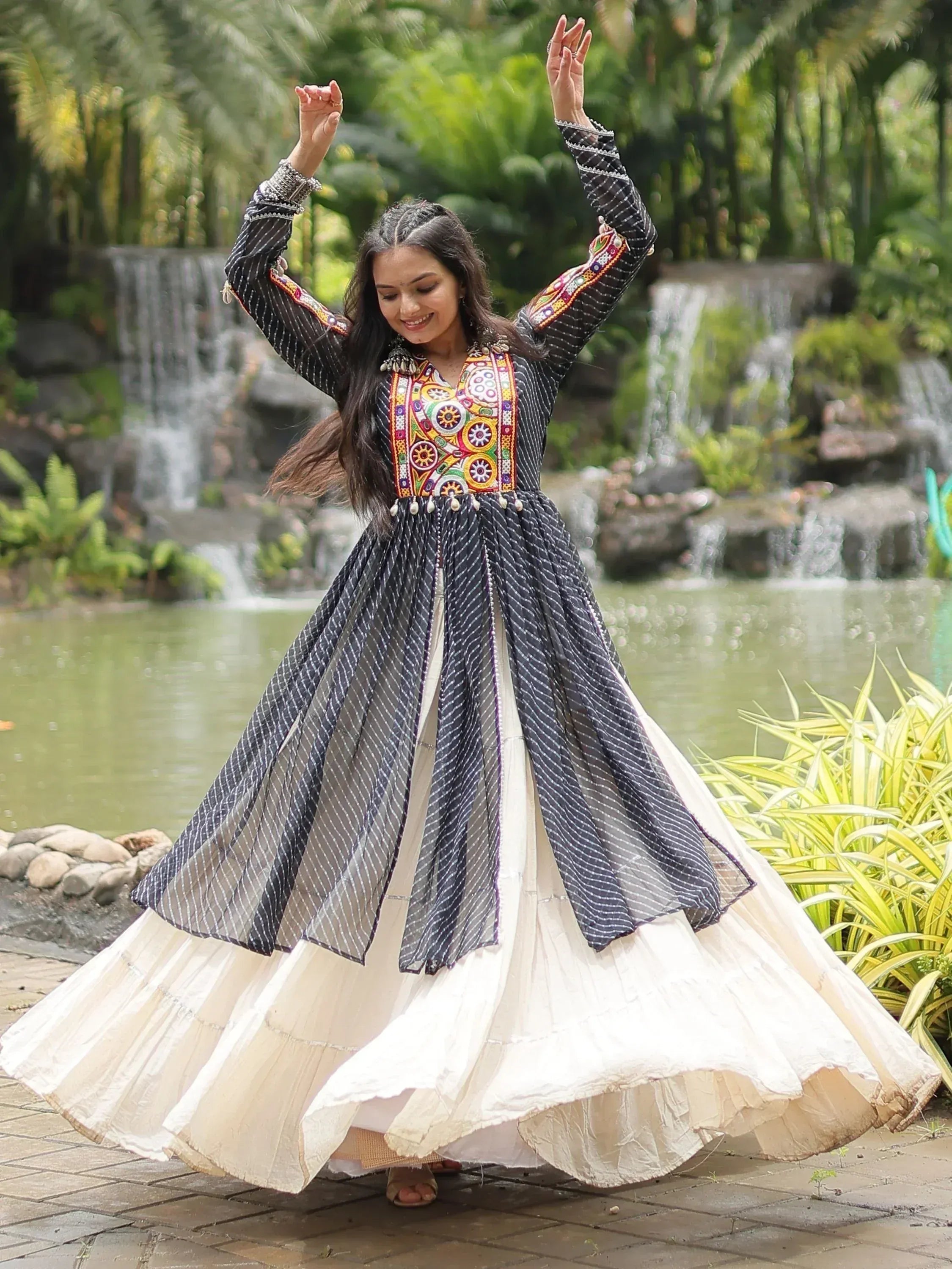 Woman twirling in black and white ethnic gown with colorful embroidery, garden backdrop