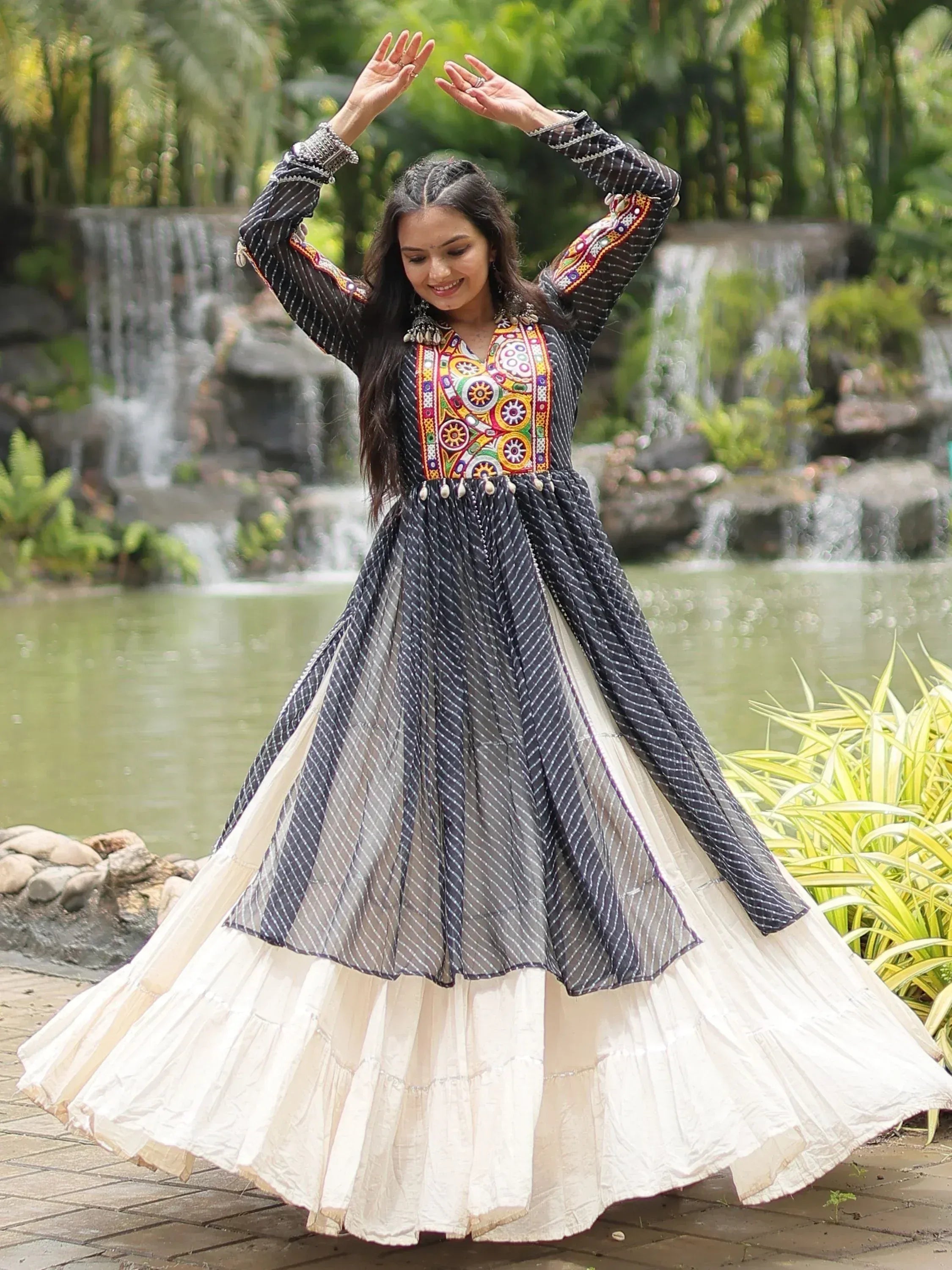 Woman in black and white striped ethnic gown with colorful embroidery, dancing near waterfall