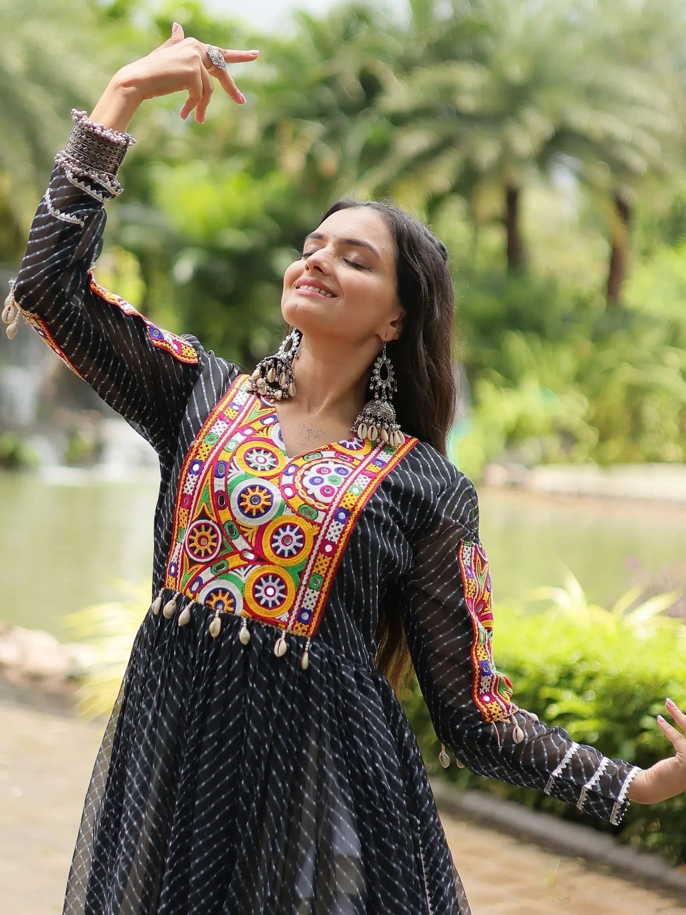 Woman in black ethnic gown with colorful embroidery and mirror work, dancing outdoors