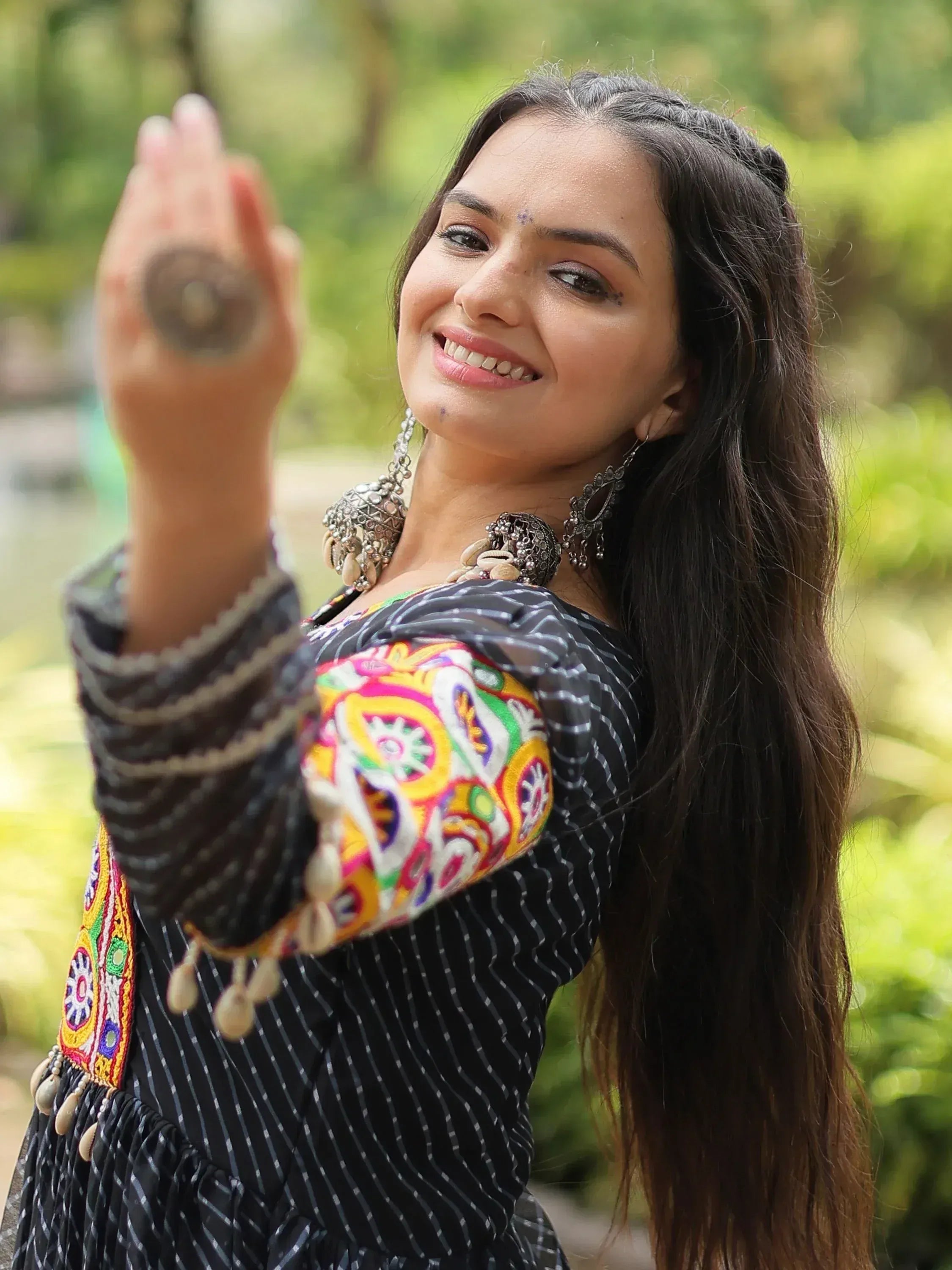 Woman in black striped ethnic dress with colorful embroidery and traditional jewelry, smiling outdoors