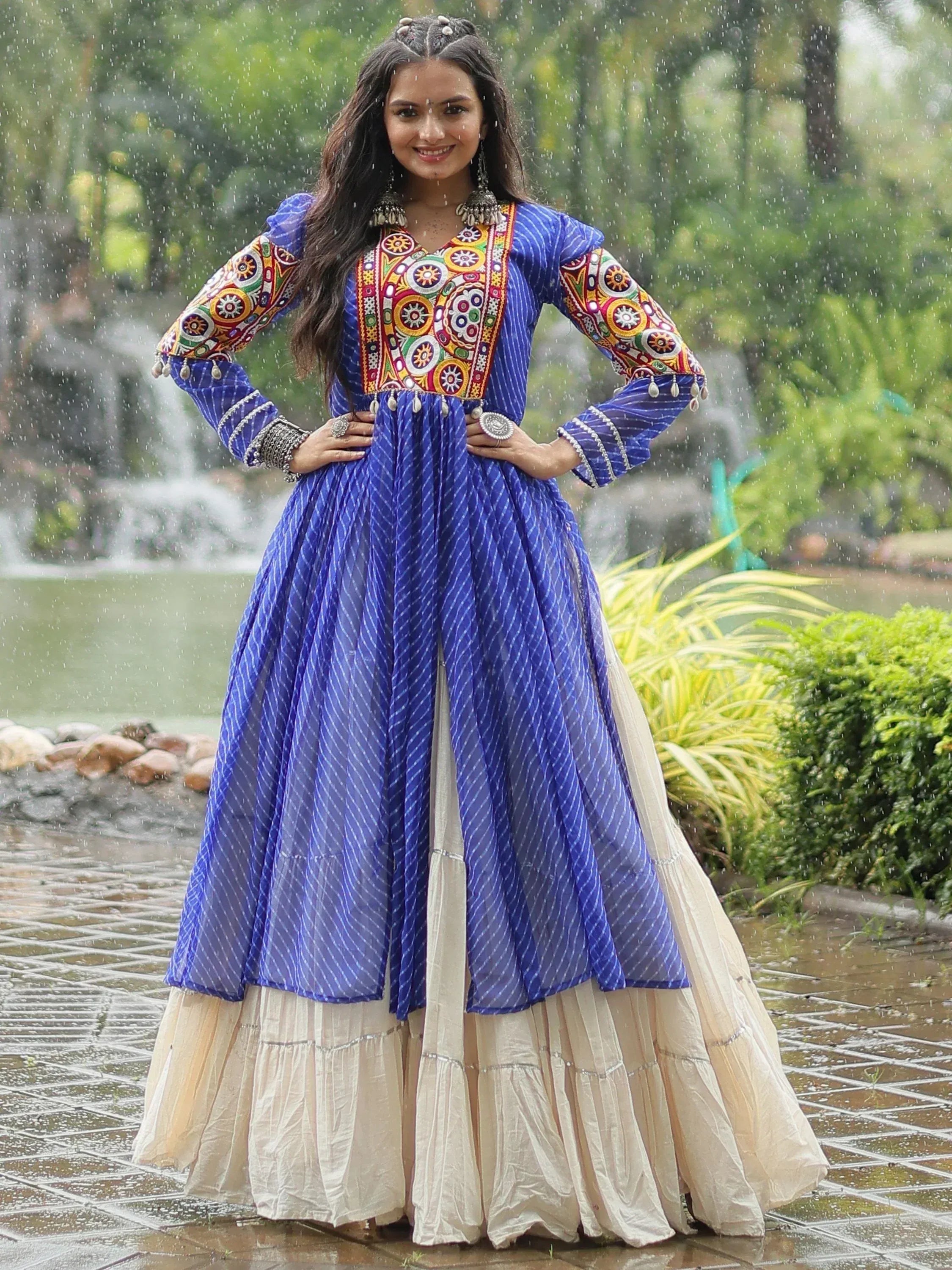 Blue embroidered ethnic gown with colorful mirror work, paired with cream skirt, worn in rainy garden setting