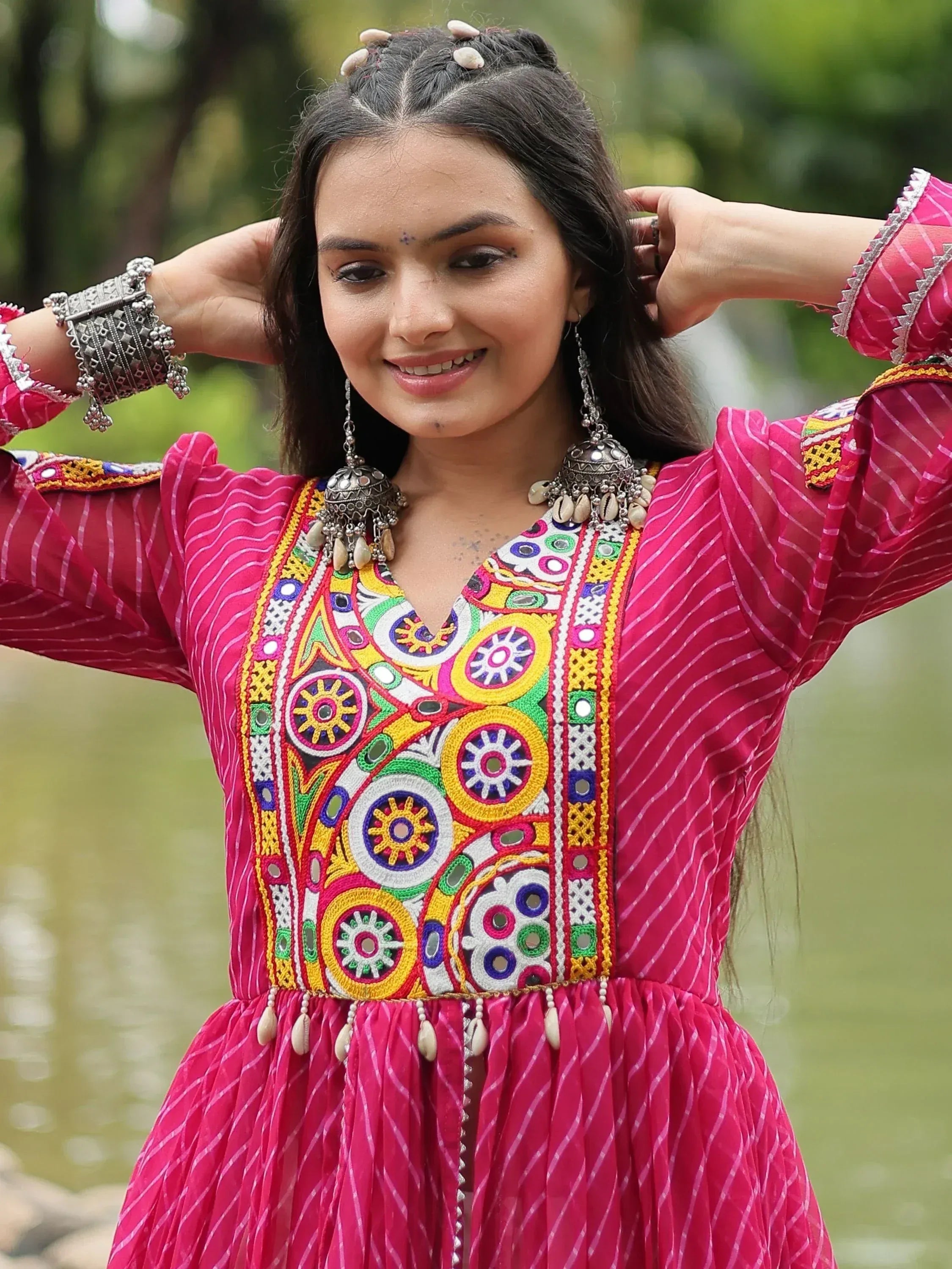 Woman in vibrant pink ethnic gown with colorful embroidery and traditional jewelry