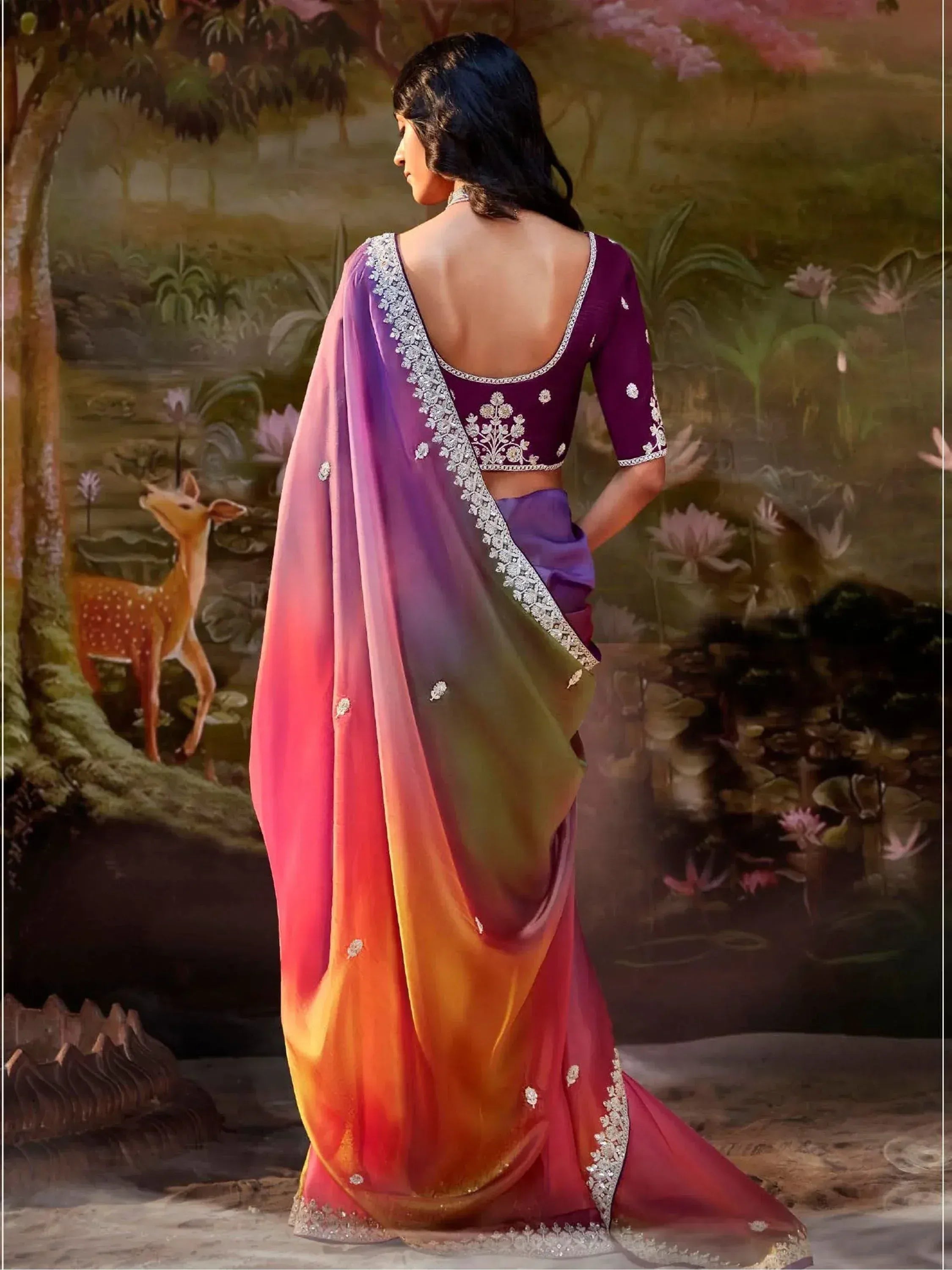Woman in vibrant ombre saree with floral embroidery, purple blouse, and scenic backdrop