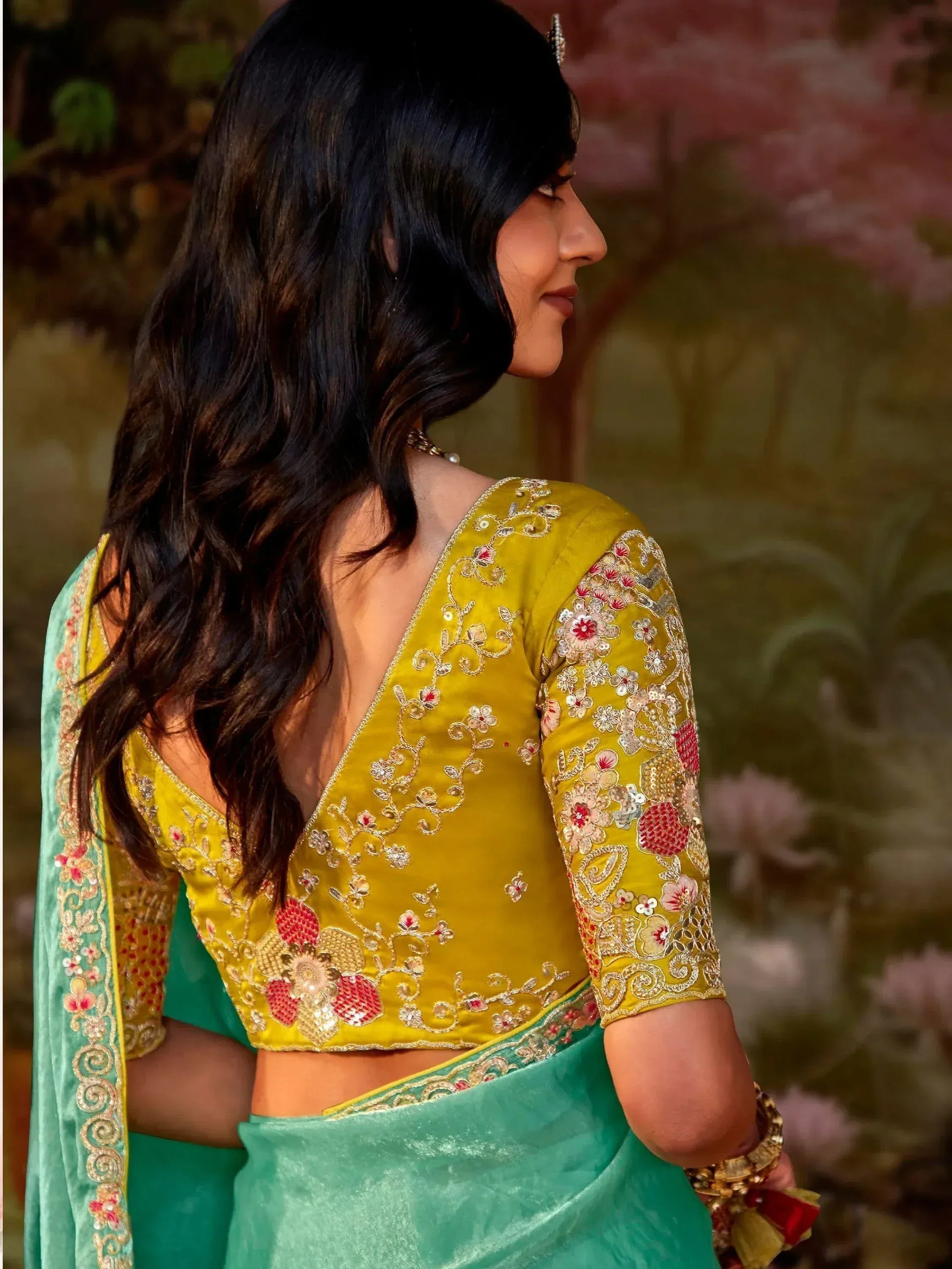 Woman in mustard yellow embroidered blouse with green saree, floral detailing, and backless design