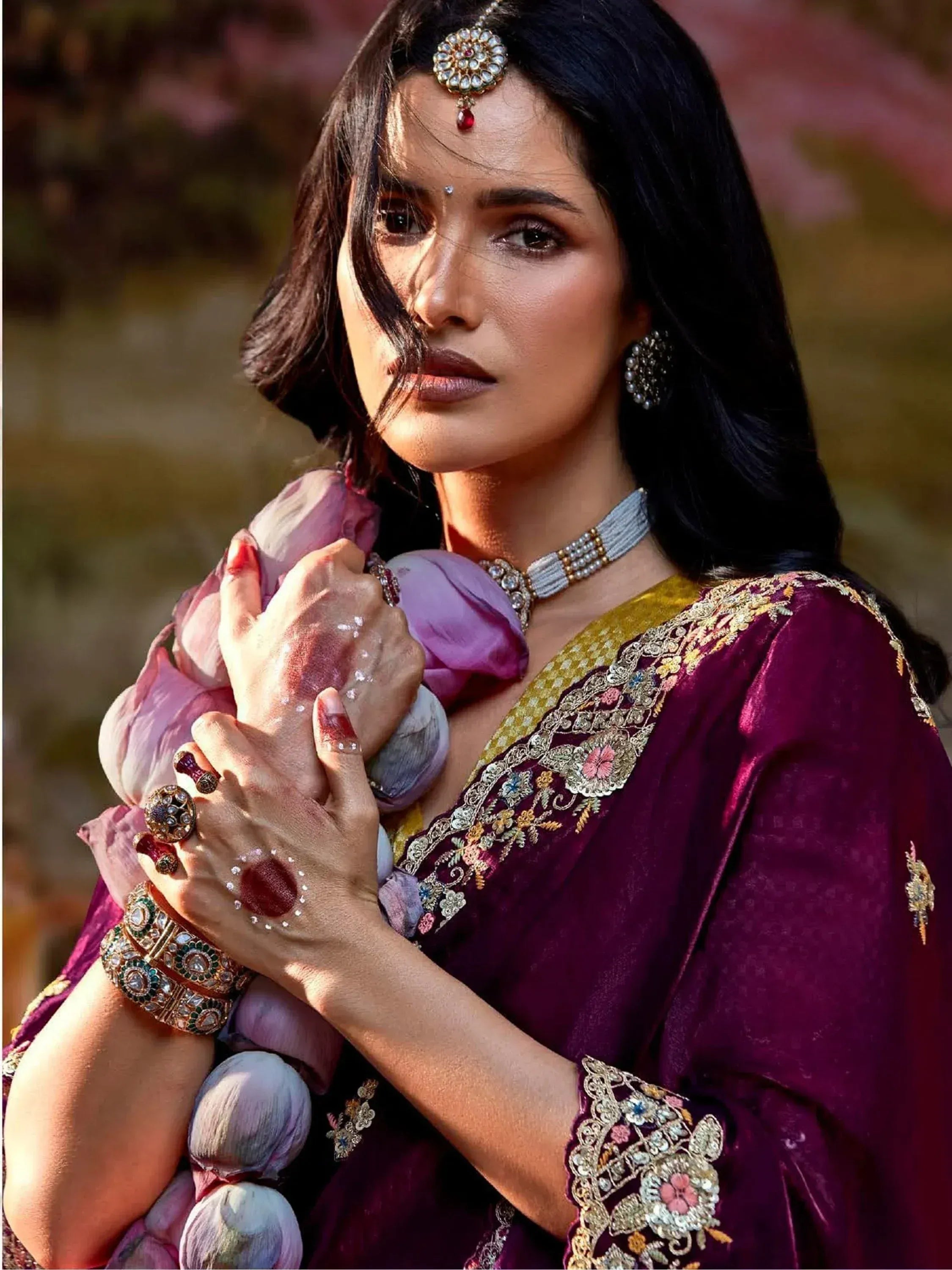 Woman in maroon embroidered ethnic gown with floral details, traditional jewelry, and henna hands