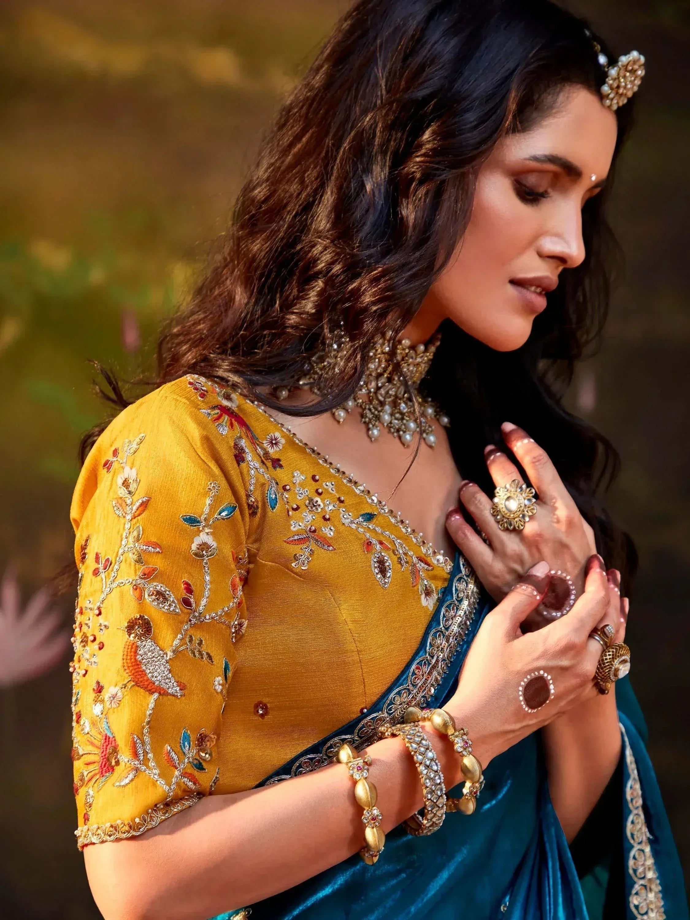 Woman in yellow embroidered blouse and teal saree with traditional Indian jewelry