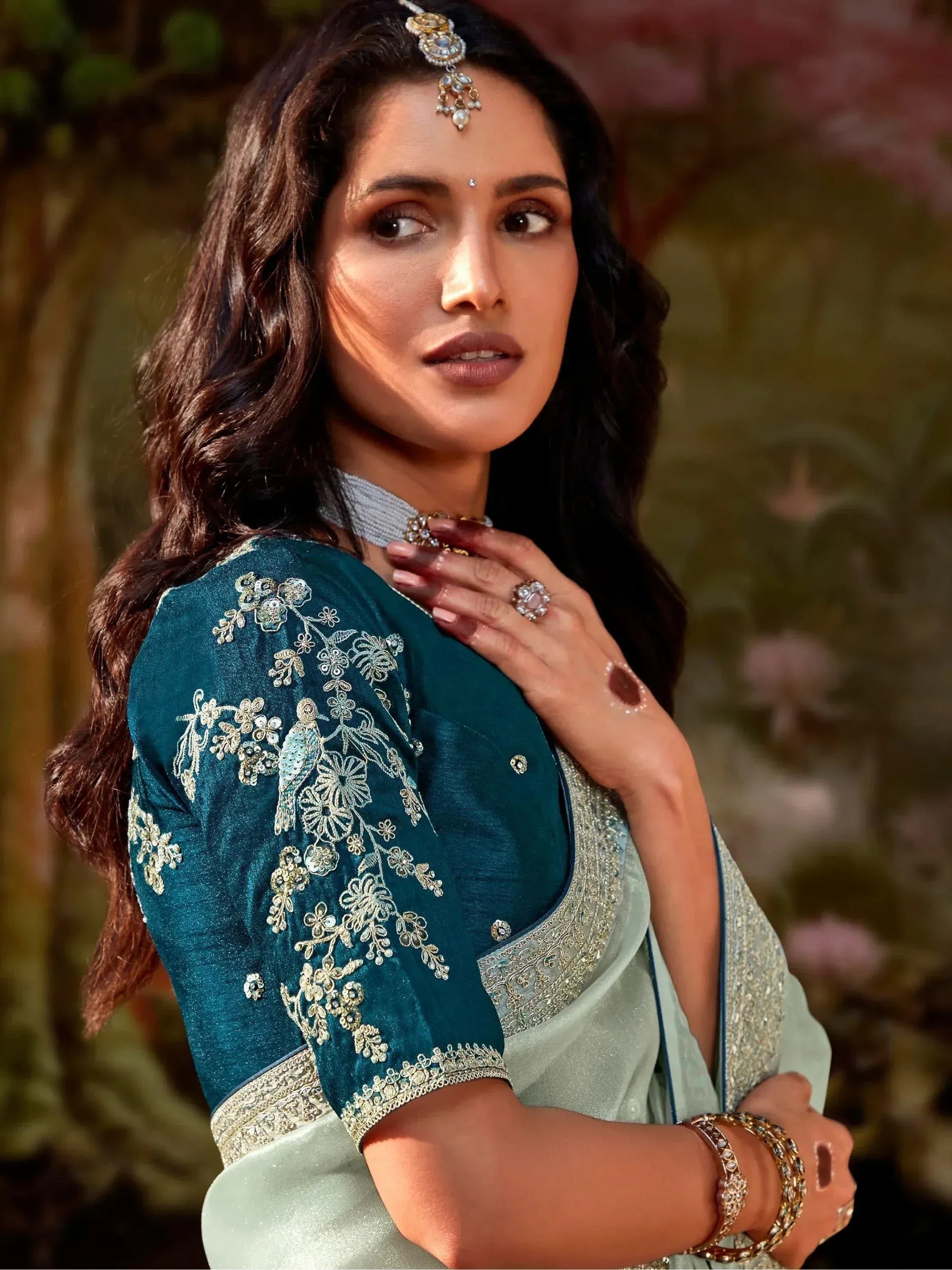 Woman in teal embroidered saree with gold floral work, traditional Indian ethnic wear for festive occasions.