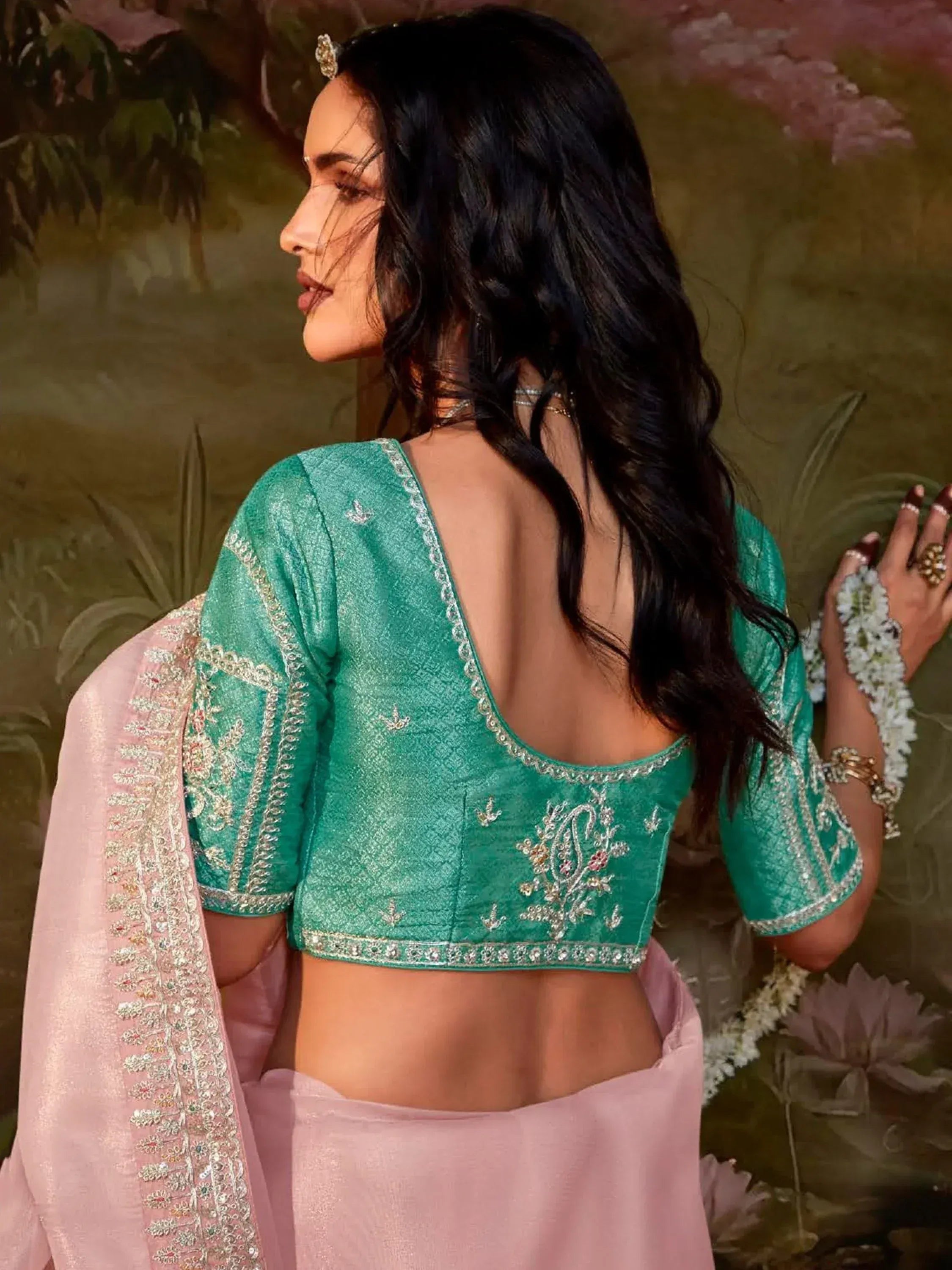 Emerald green embroidered blouse with open back, paired with pink saree, showcasing Indian ethnic wear design.
