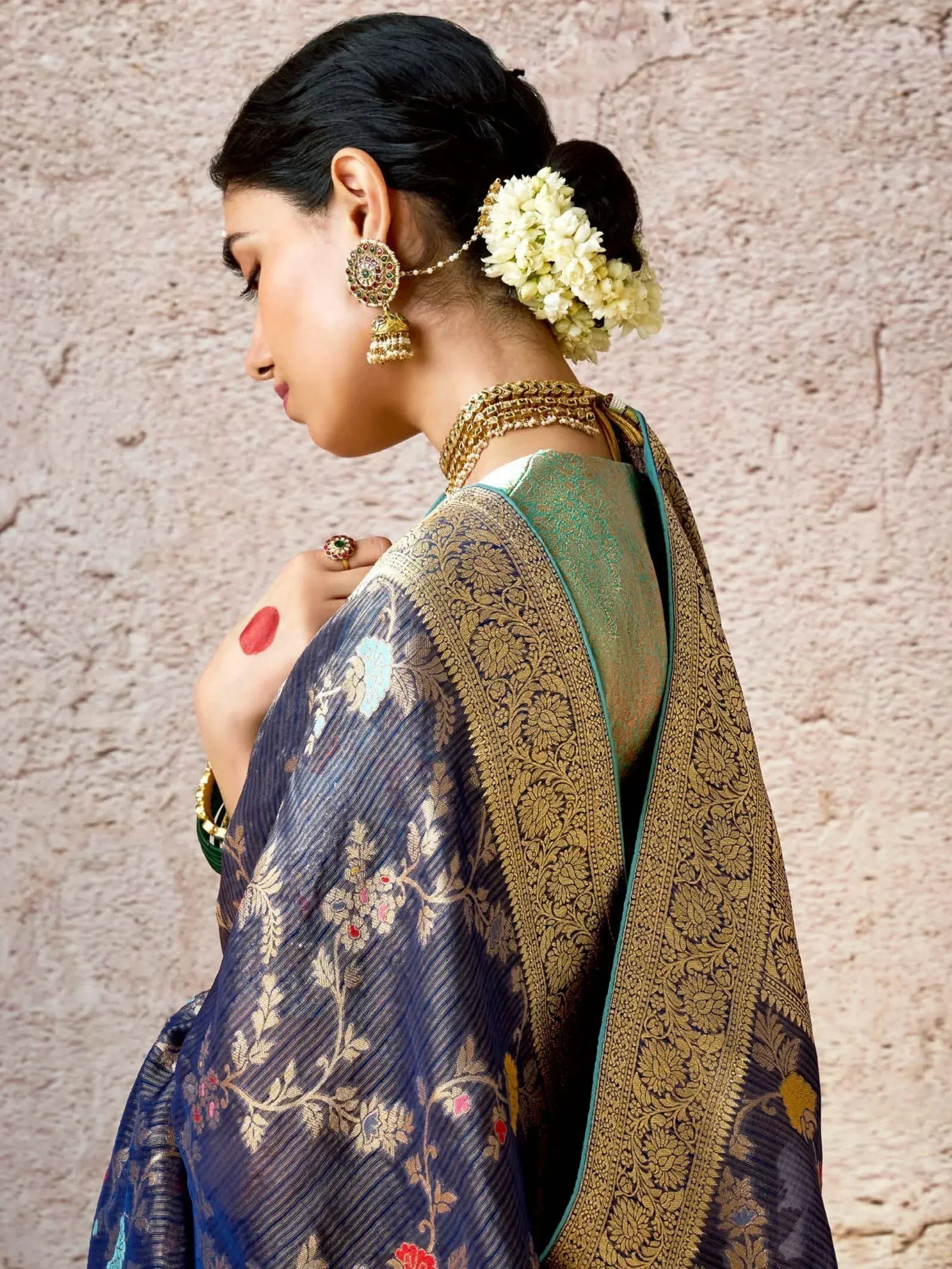 Woman in elegant blue and gold embroidered saree with floral hair accessory and traditional jewelry