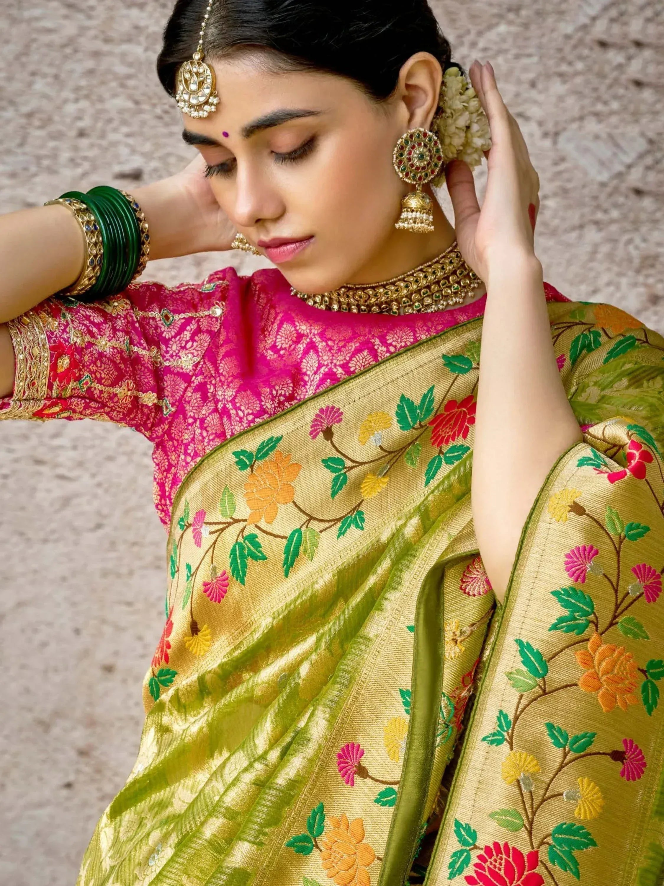 Woman in vibrant floral saree with pink blouse, traditional jewelry, and green bangles, showcasing Indian ethnic wear.