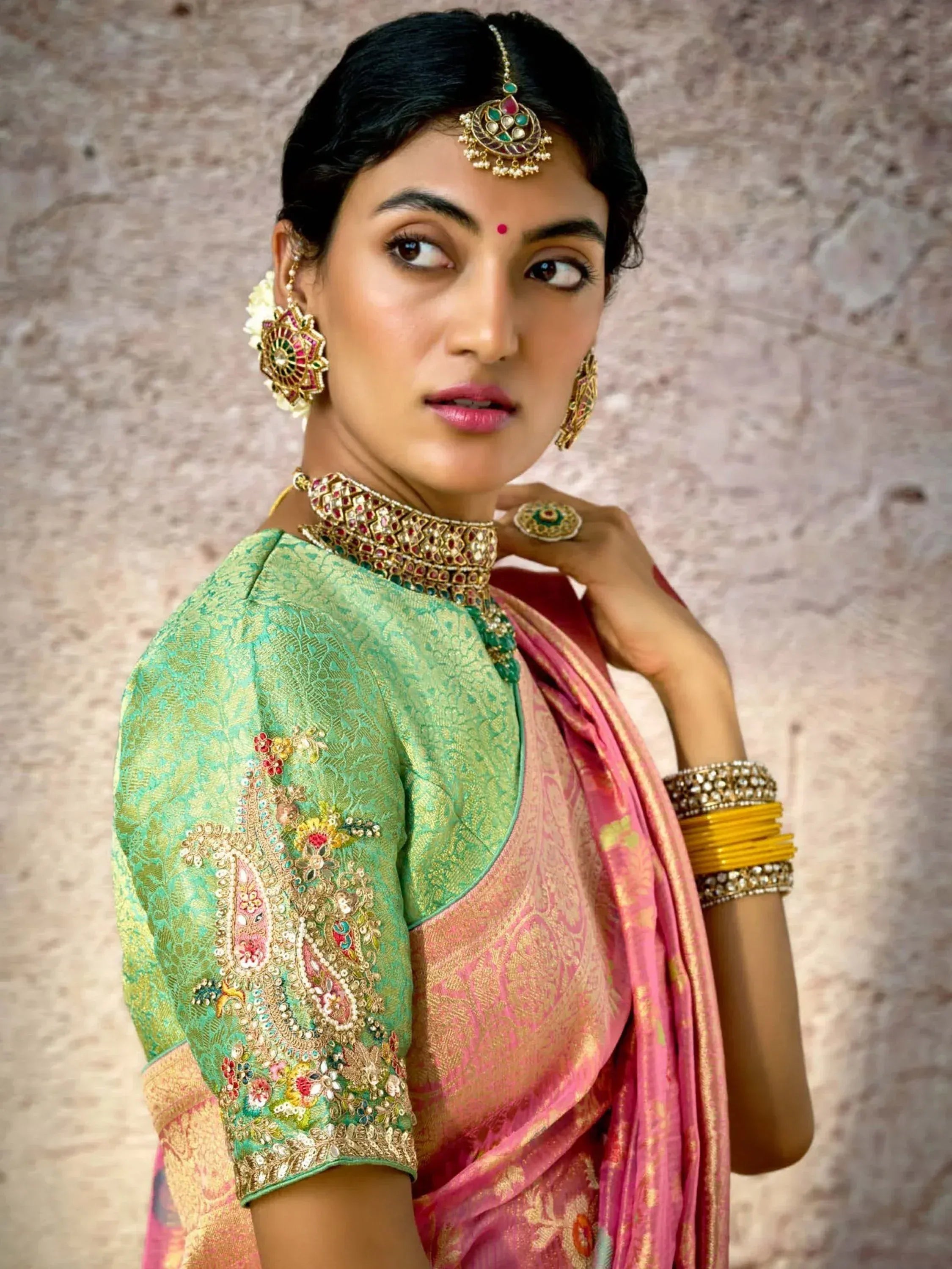 Woman in green embroidered blouse and pink saree with traditional Indian jewelry