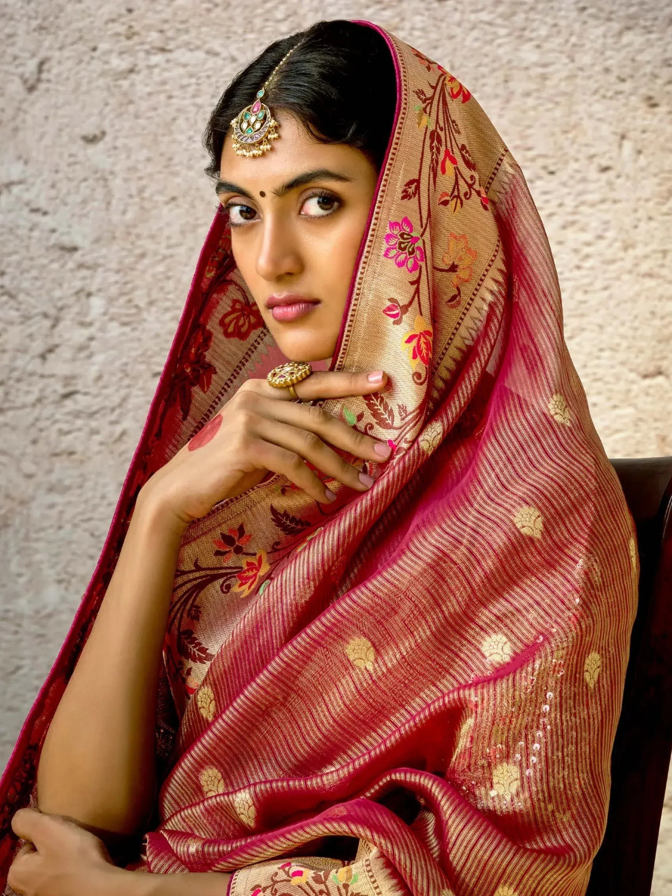 Woman in elegant red and gold floral saree with traditional jewelry, showcasing Indian ethnic wear