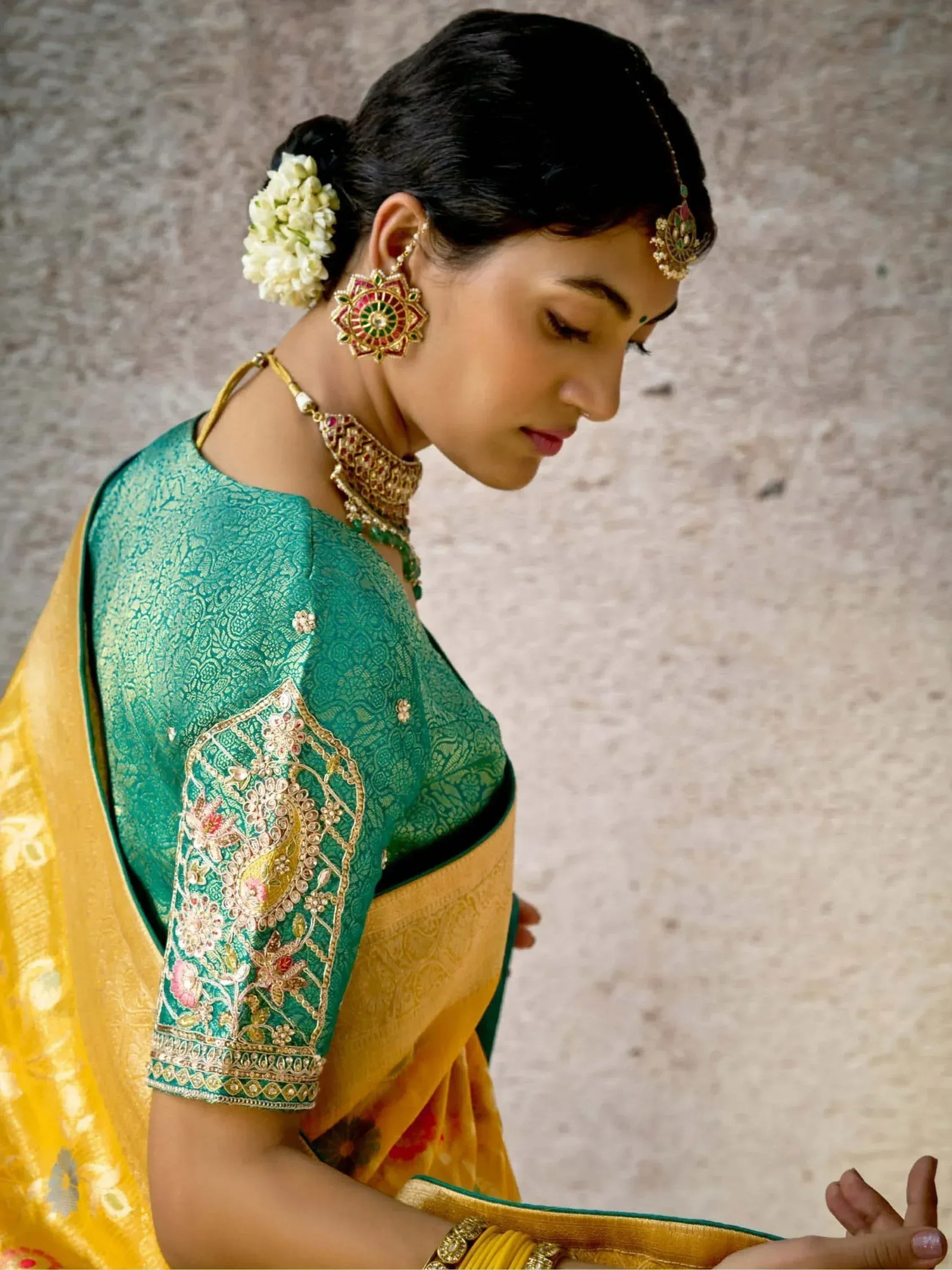 Woman in green and gold embroidered saree with traditional jewelry and floral hair accessory