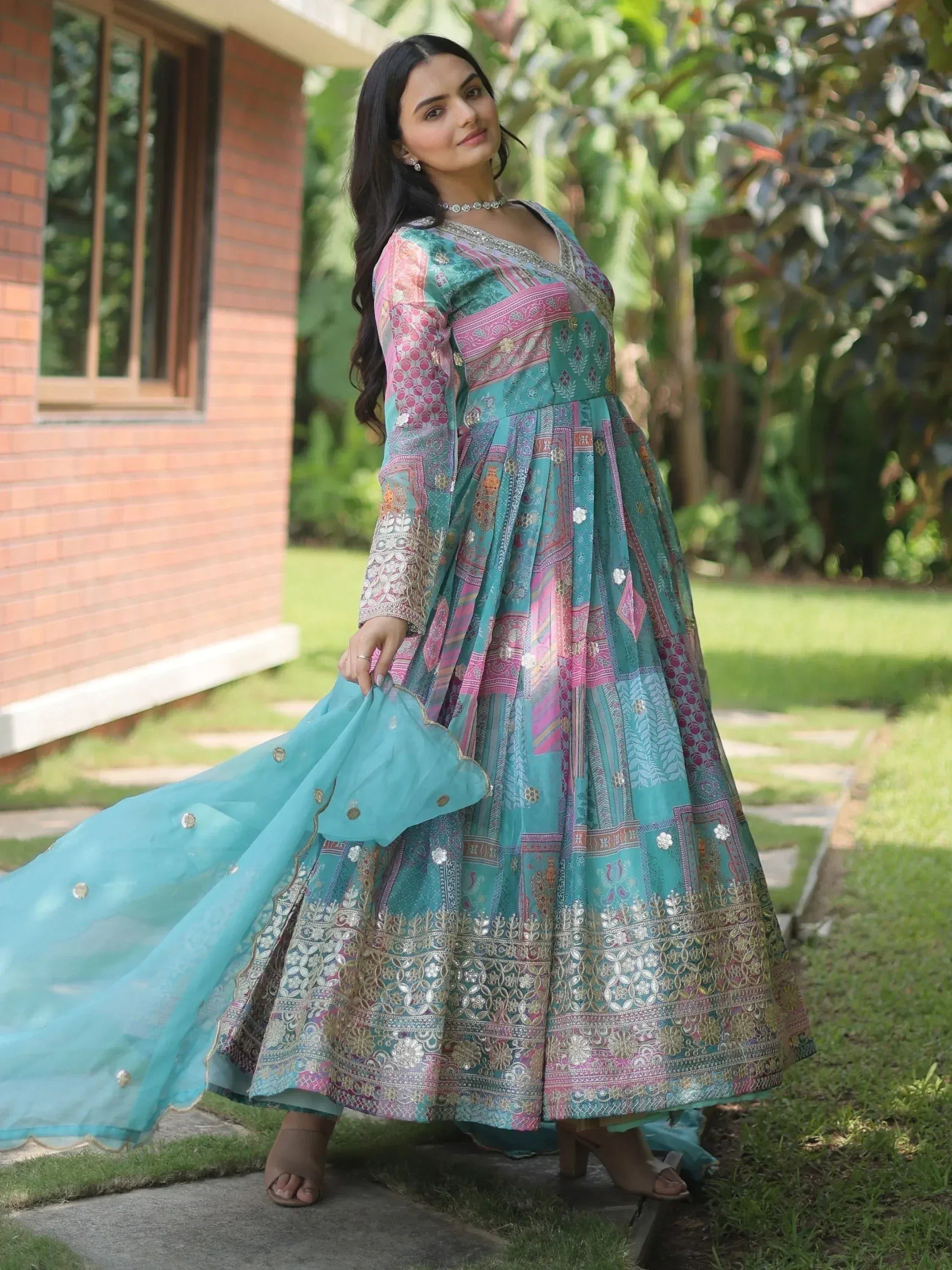 Woman in teal and pink printed ethnic gown with embroidery, perfect for Indian festive occasions.