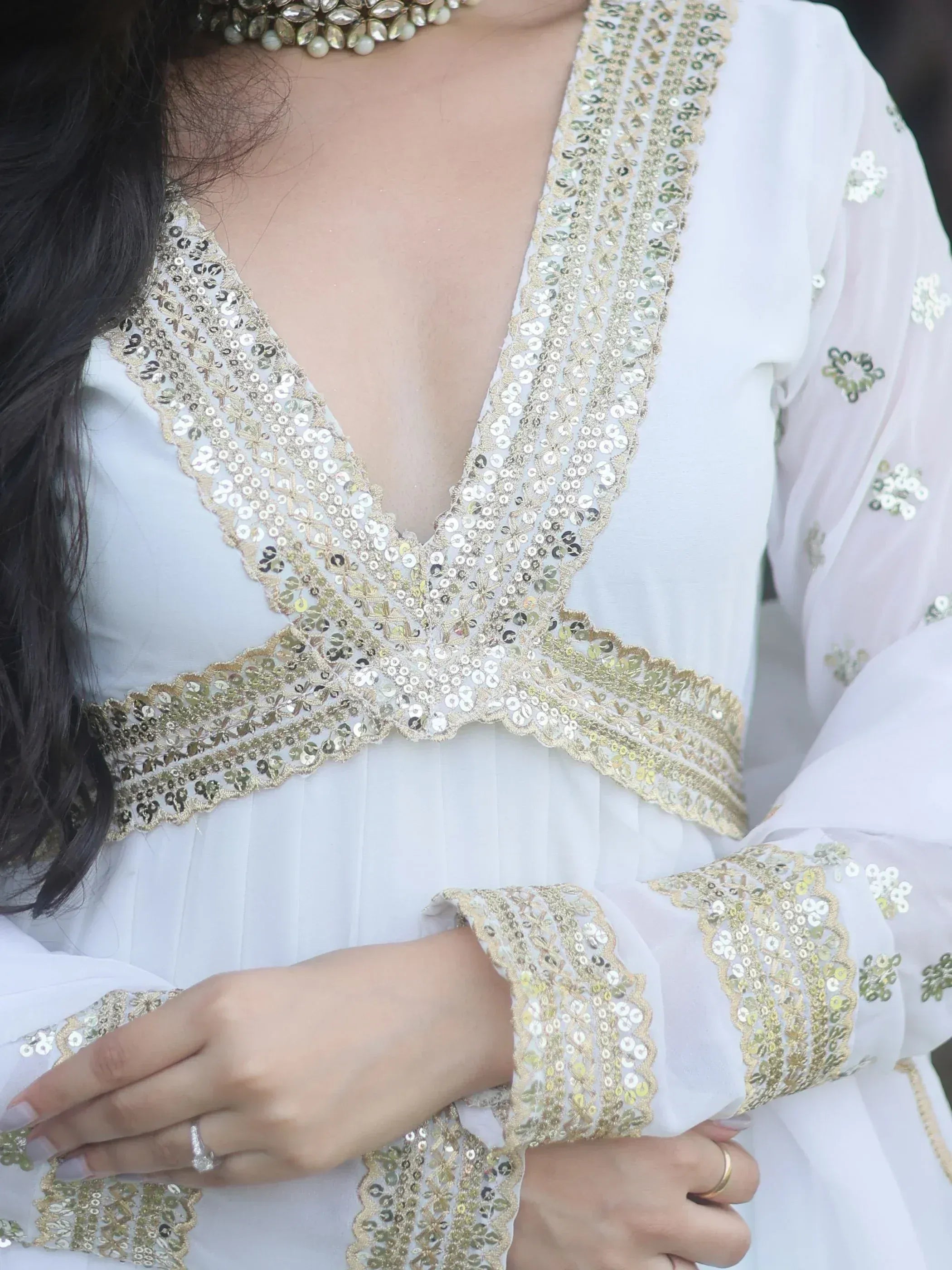 White ethnic gown with gold sequin embroidery, V-neckline, and embellished sleeves for festive occasions.