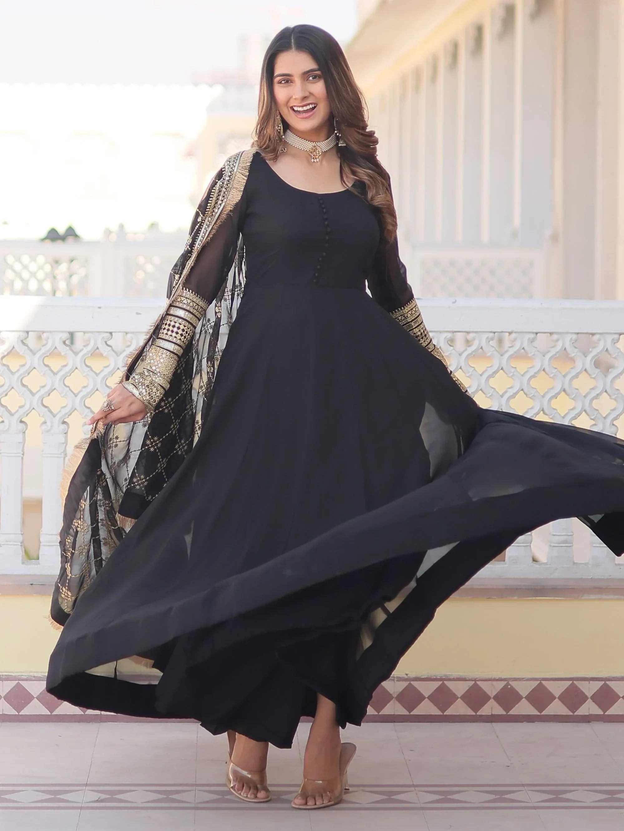 Woman in flowing black Anarkali gown with gold embroidered dupatta, standing outdoors