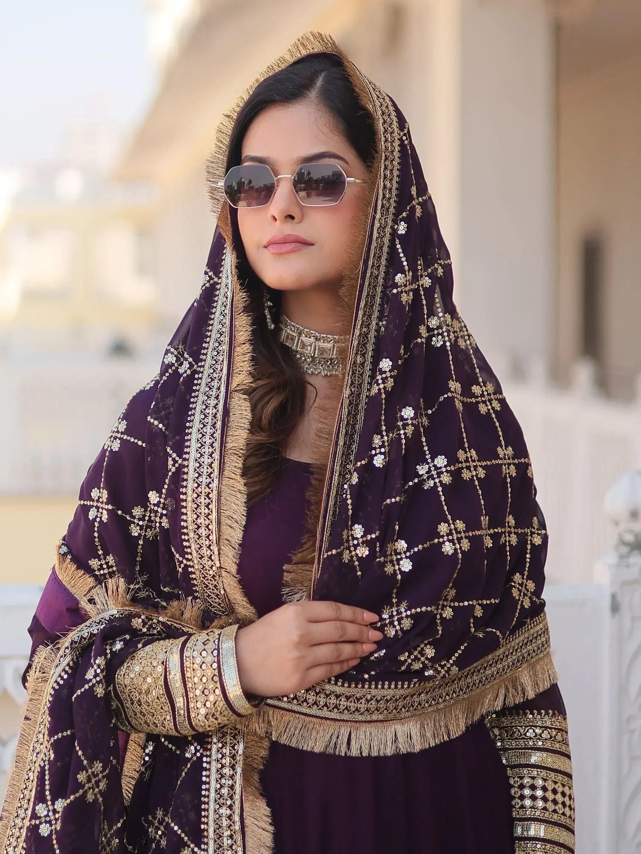 Elegant purple ethnic wear with gold embroidery and fringe, styled with sunglasses for a modern look.