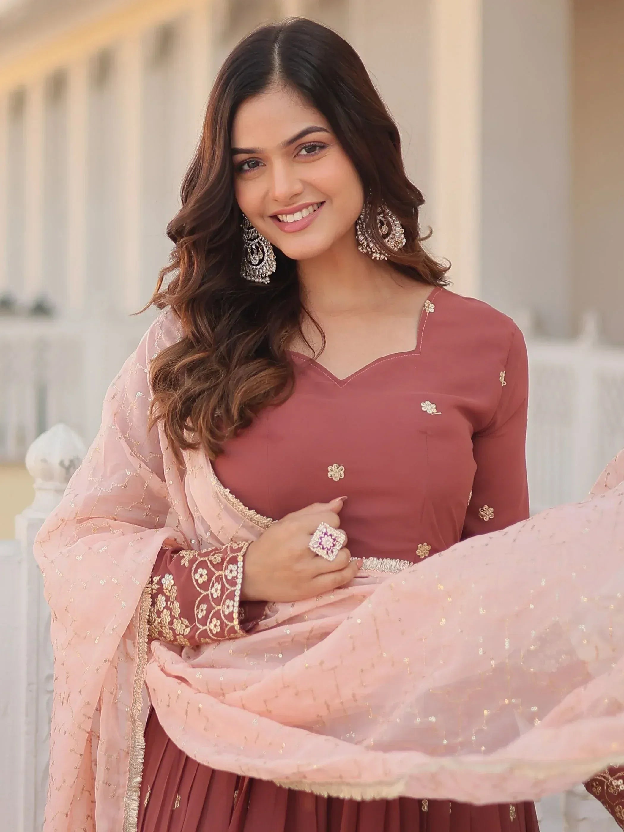 Woman in elegant maroon salwar kameez with pink dupatta, floral embroidery, and statement jewelry