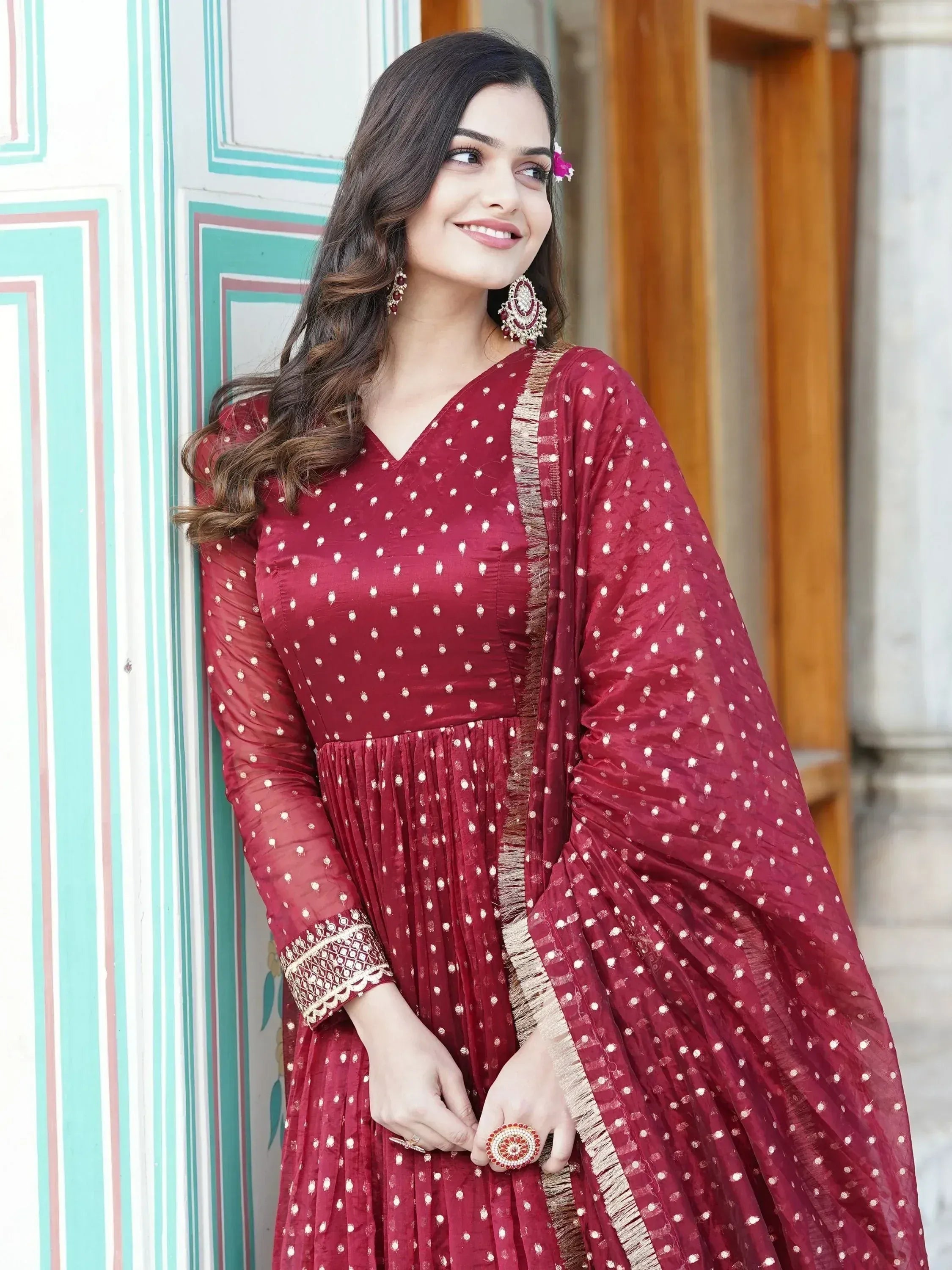 Maroon ethnic gown with white polka dots and gold trim, styled with traditional jewelry for Indian occasions