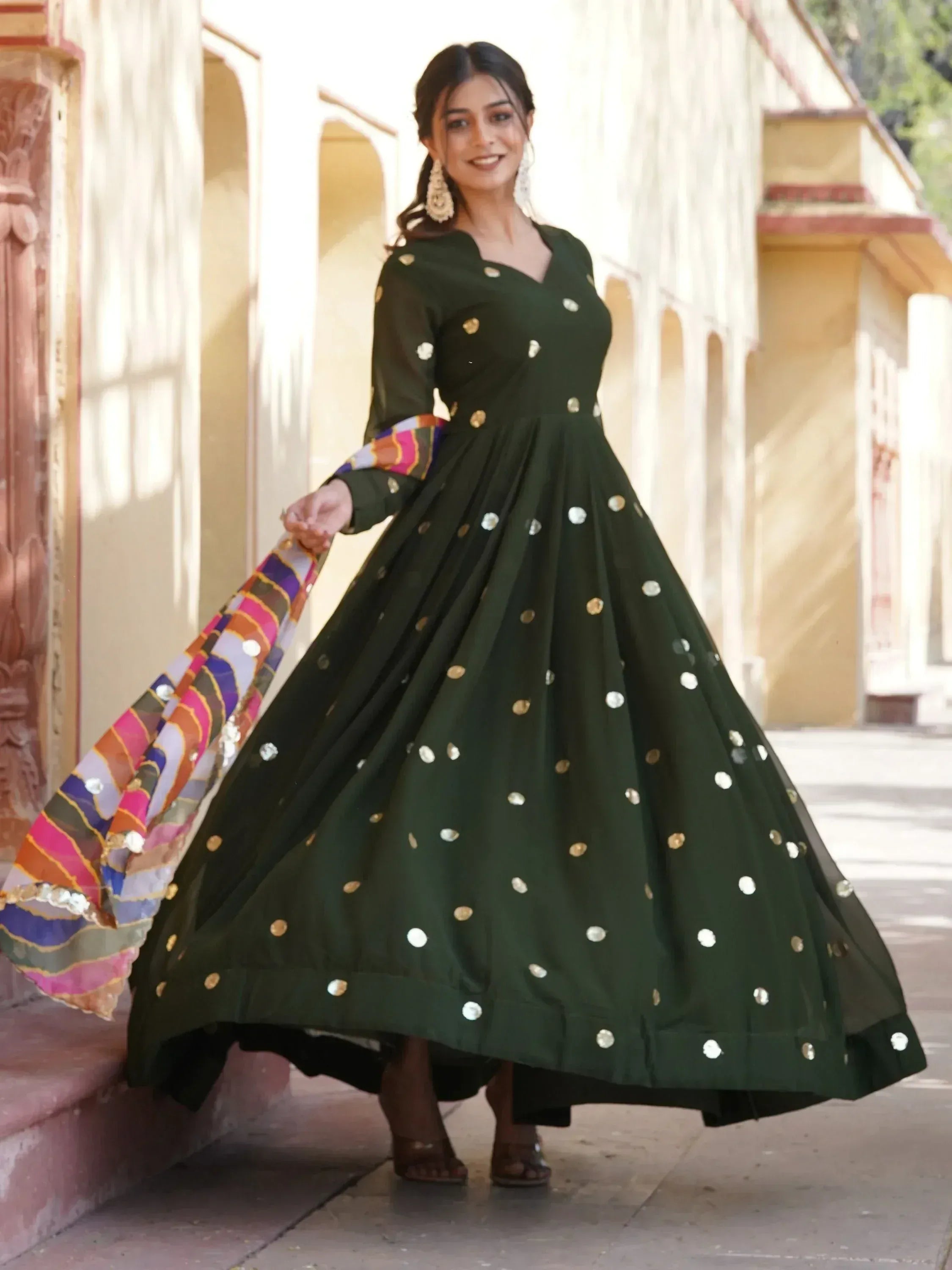 Woman in green ethnic gown with gold and silver mirror work, holding colorful dupatta, perfect for Indian occasions.