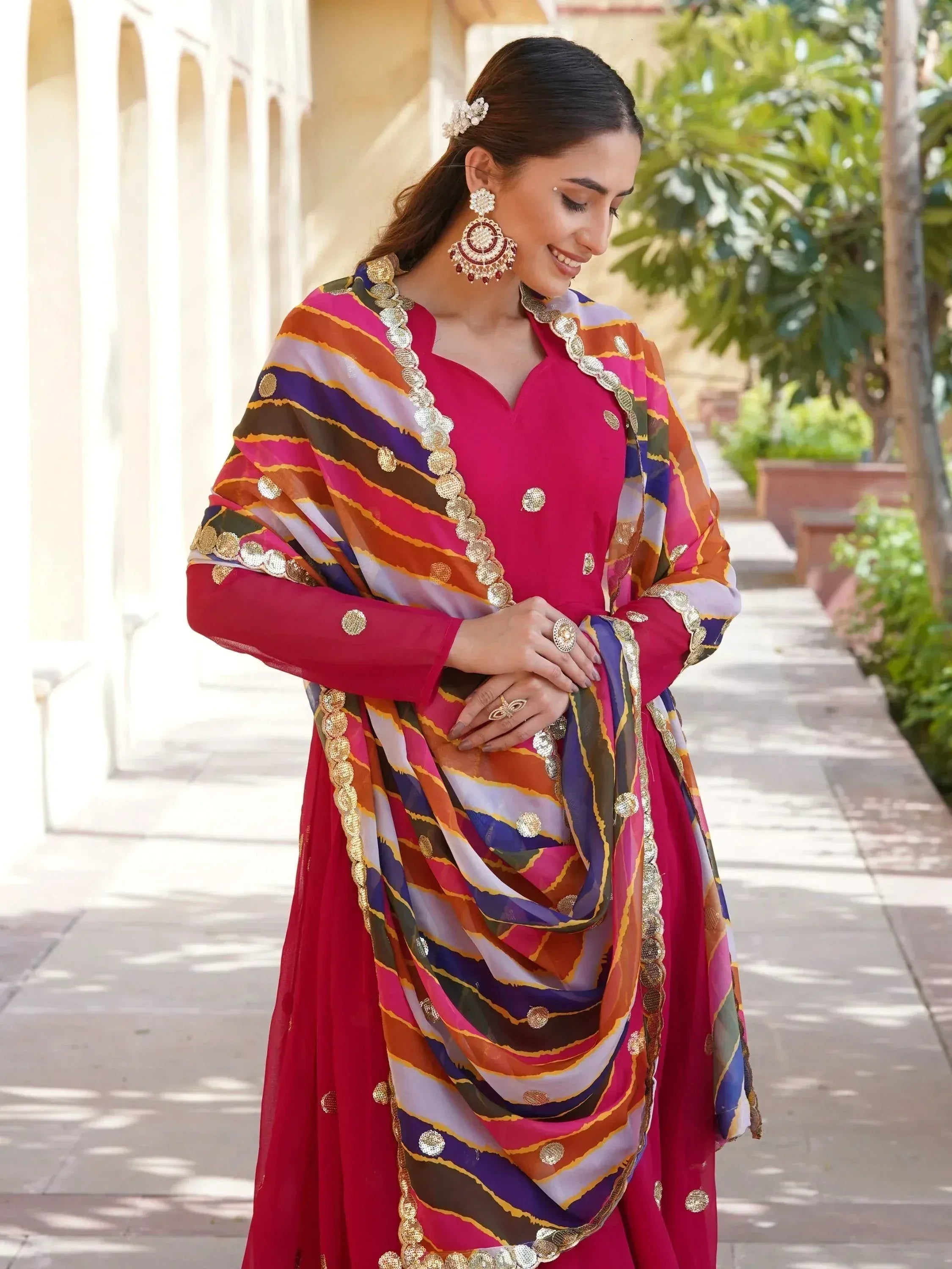 Woman in vibrant pink Indian ethnic salwar kameez with colorful striped dupatta and gold embellishments