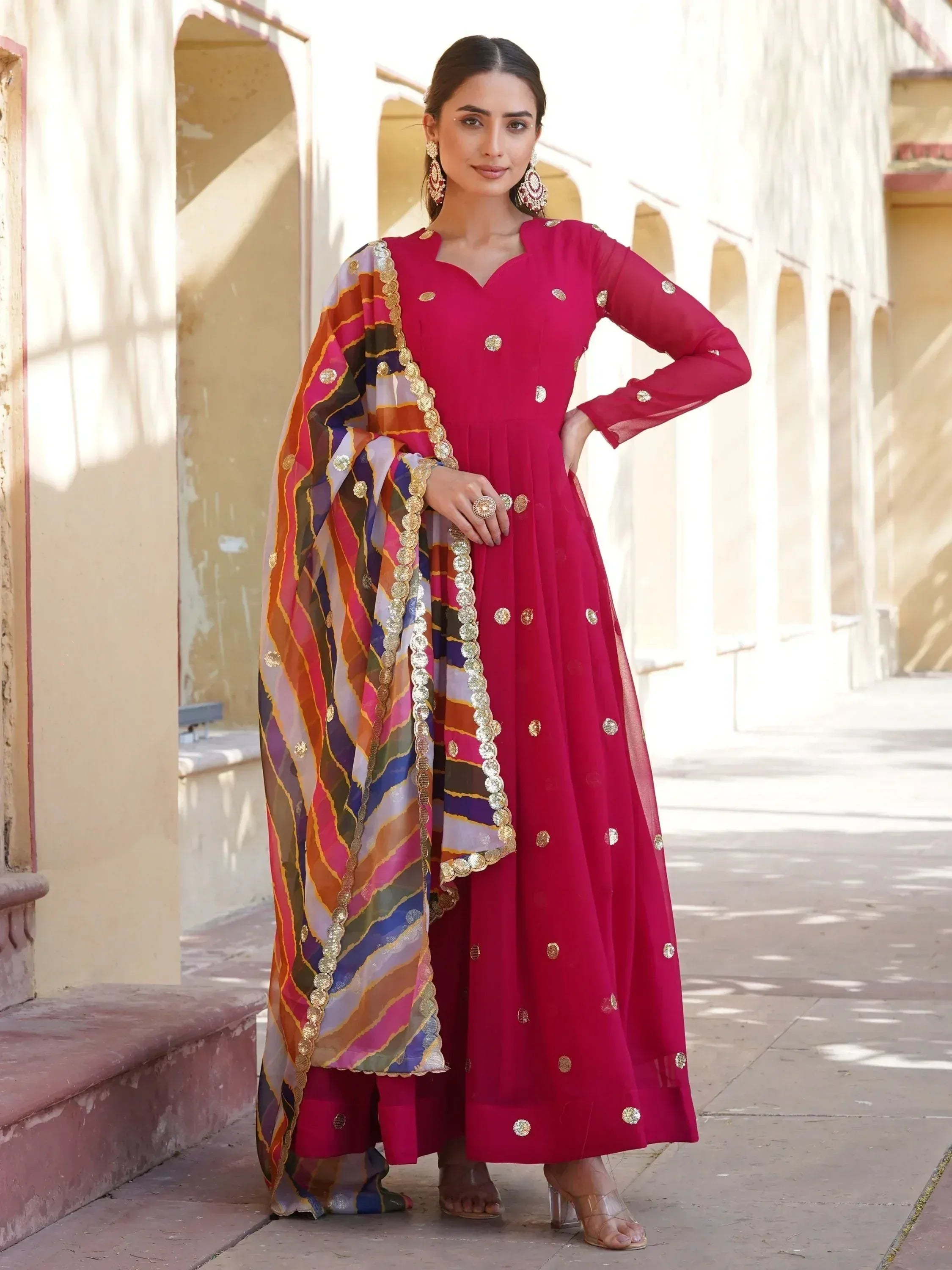 Woman in vibrant pink Indian ethnic anarkali with gold embellishments and colorful dupatta, perfect for festive occasions.