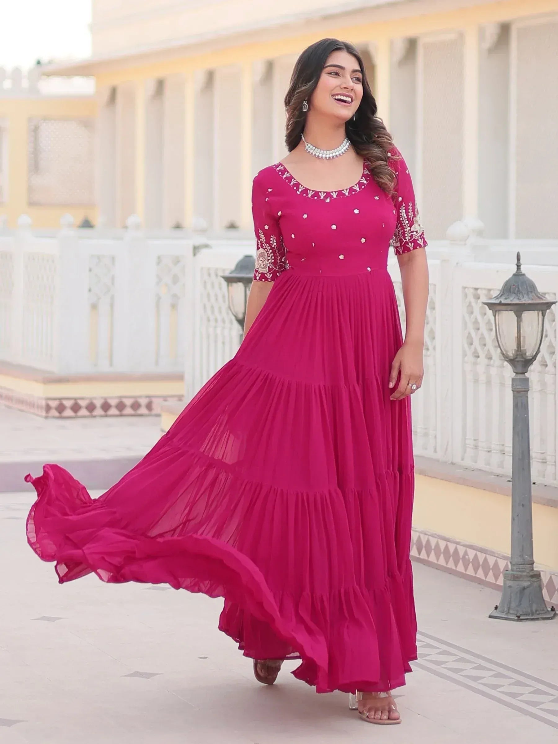 Woman in vibrant pink embroidered ethnic gown with tiered skirt, perfect for Indian festive occasions