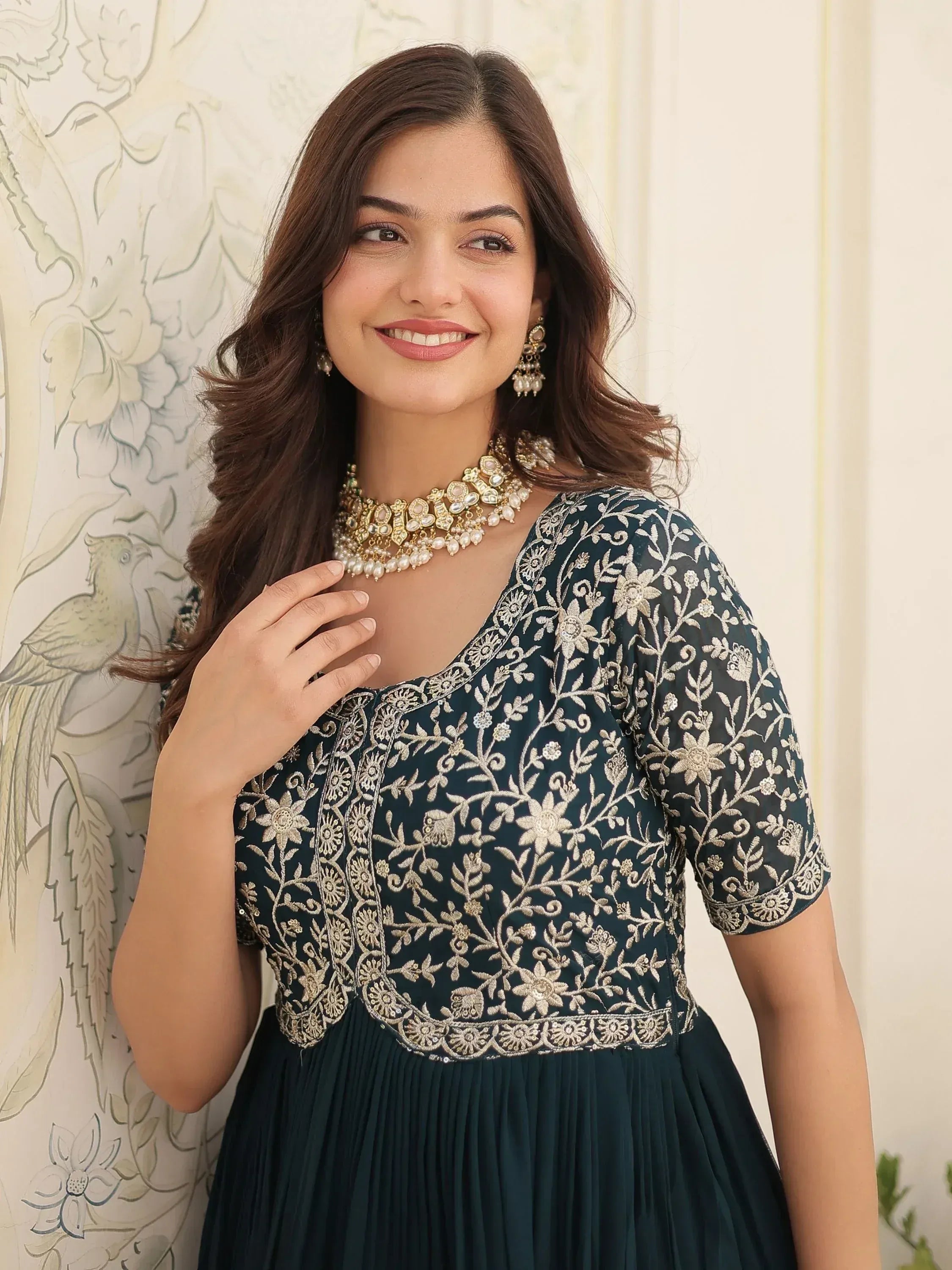 Woman in dark green embroidered ethnic gown with gold floral detailing and pearl jewelry