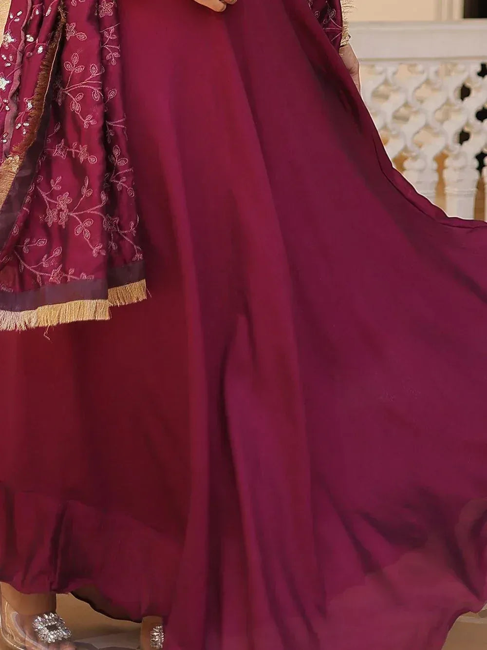 Maroon ethnic gown with floral embroidery and gold fringe, paired with embellished heels