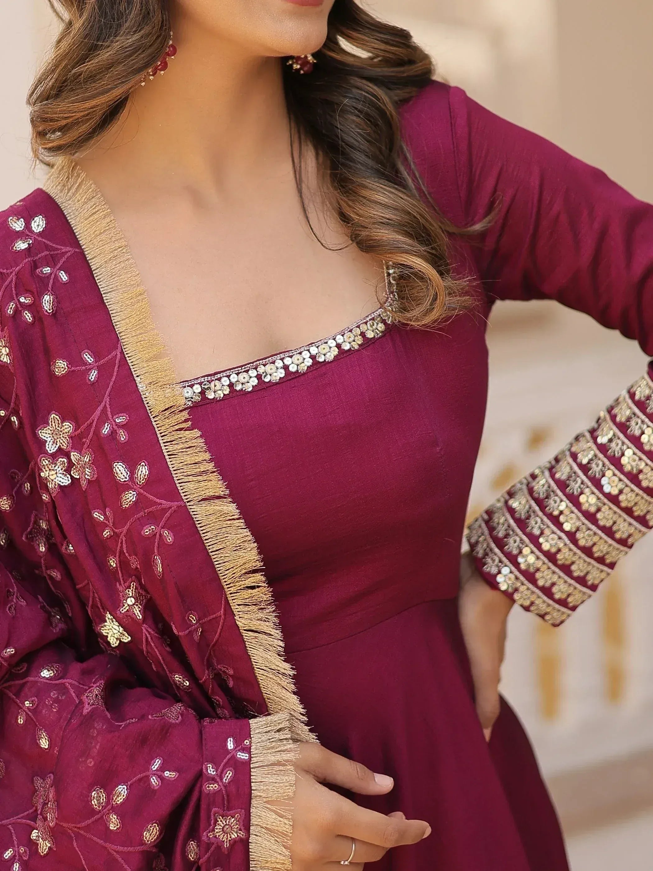 Elegant maroon ethnic gown with gold embroidery, floral motifs, and fringe detailing for Indian occasions