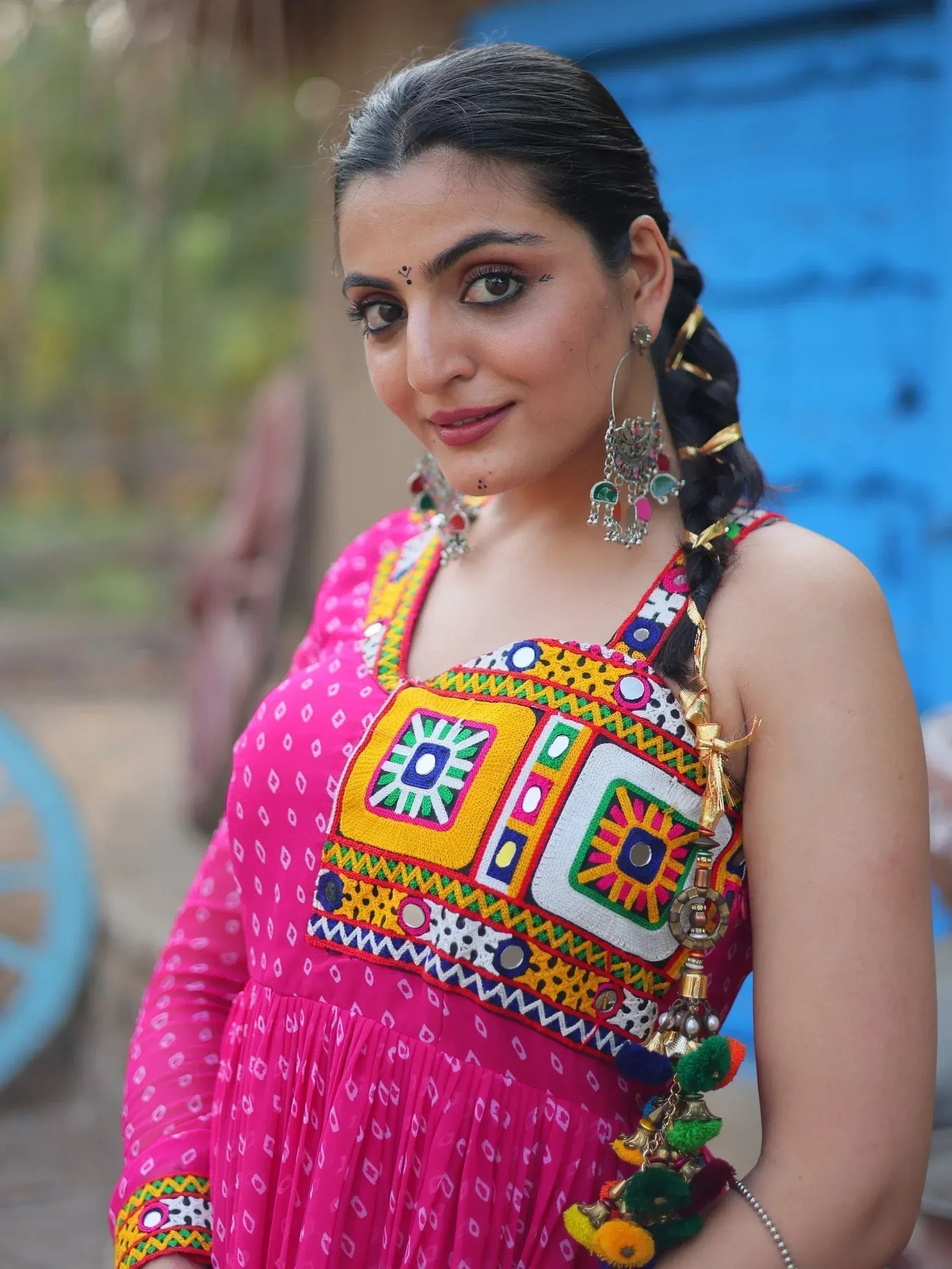Woman in vibrant pink ethnic dress with mirror work and colorful embroidery, styled with traditional jewelry