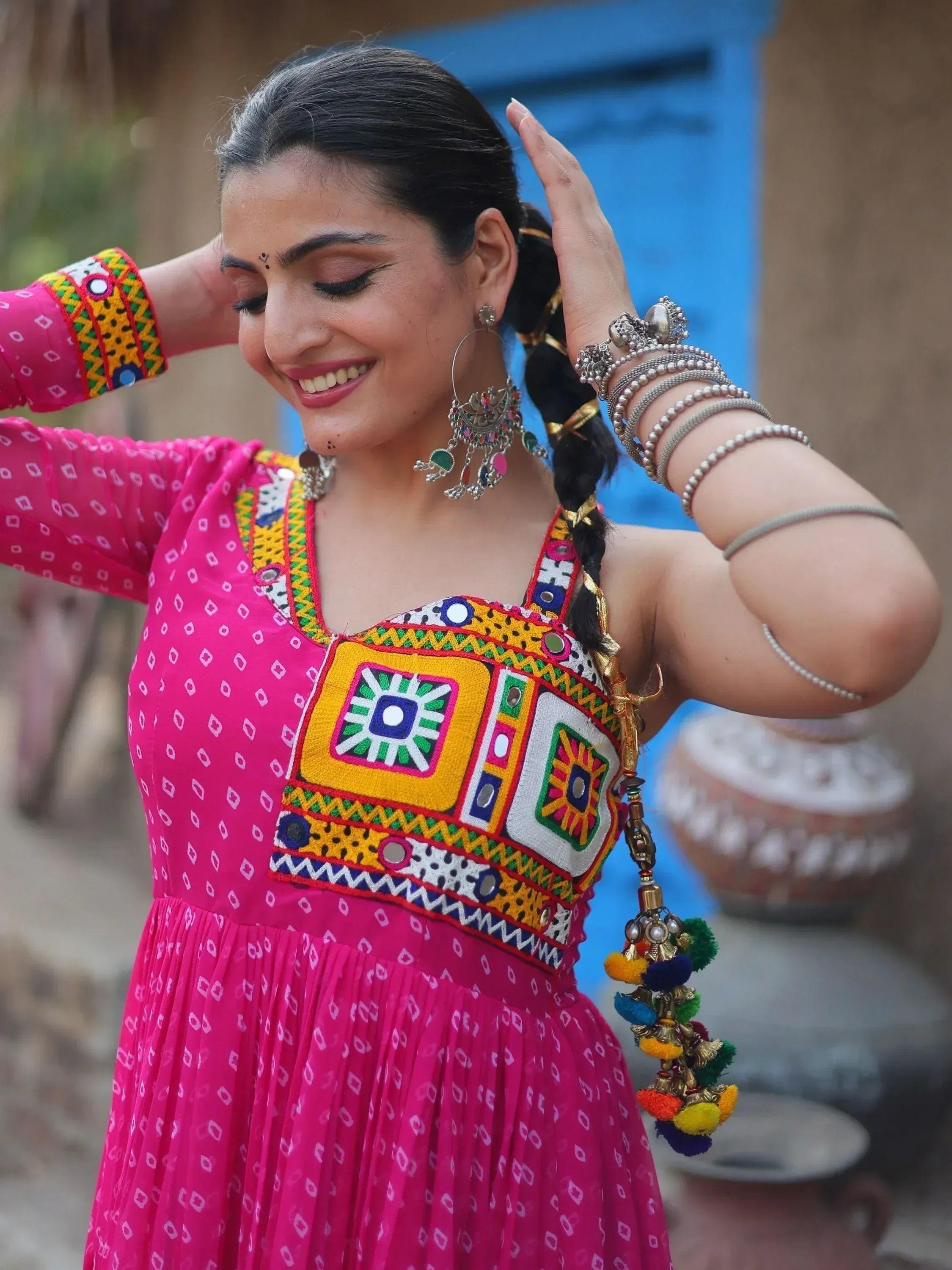Woman in vibrant pink ethnic gown with mirror work, colorful embroidery, and traditional jewelry, perfect for festive occasions.