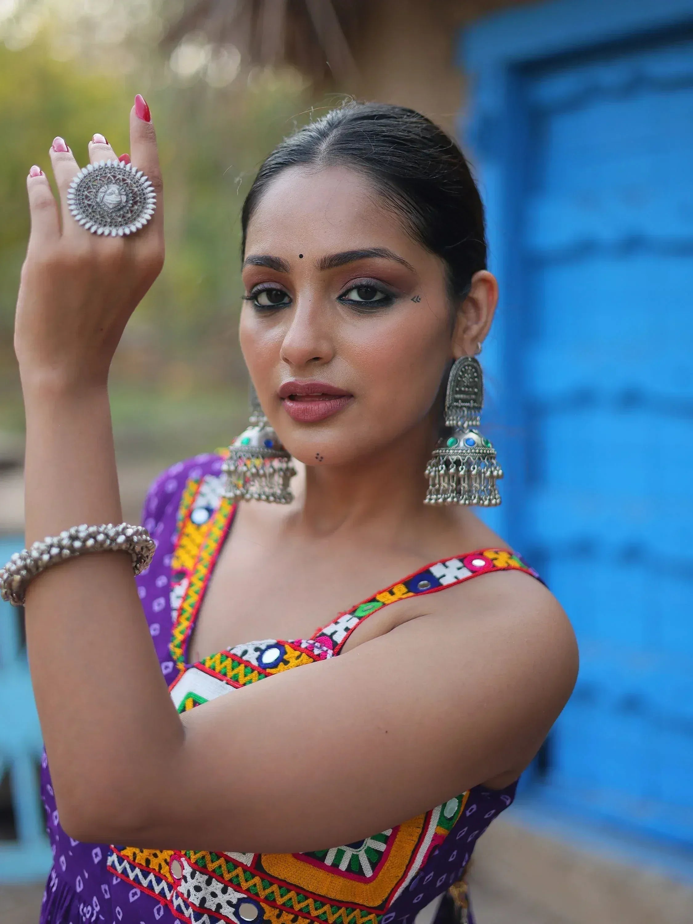 Woman in colorful embroidered ethnic top with mirror work, silver jhumka earrings, and statement ring
