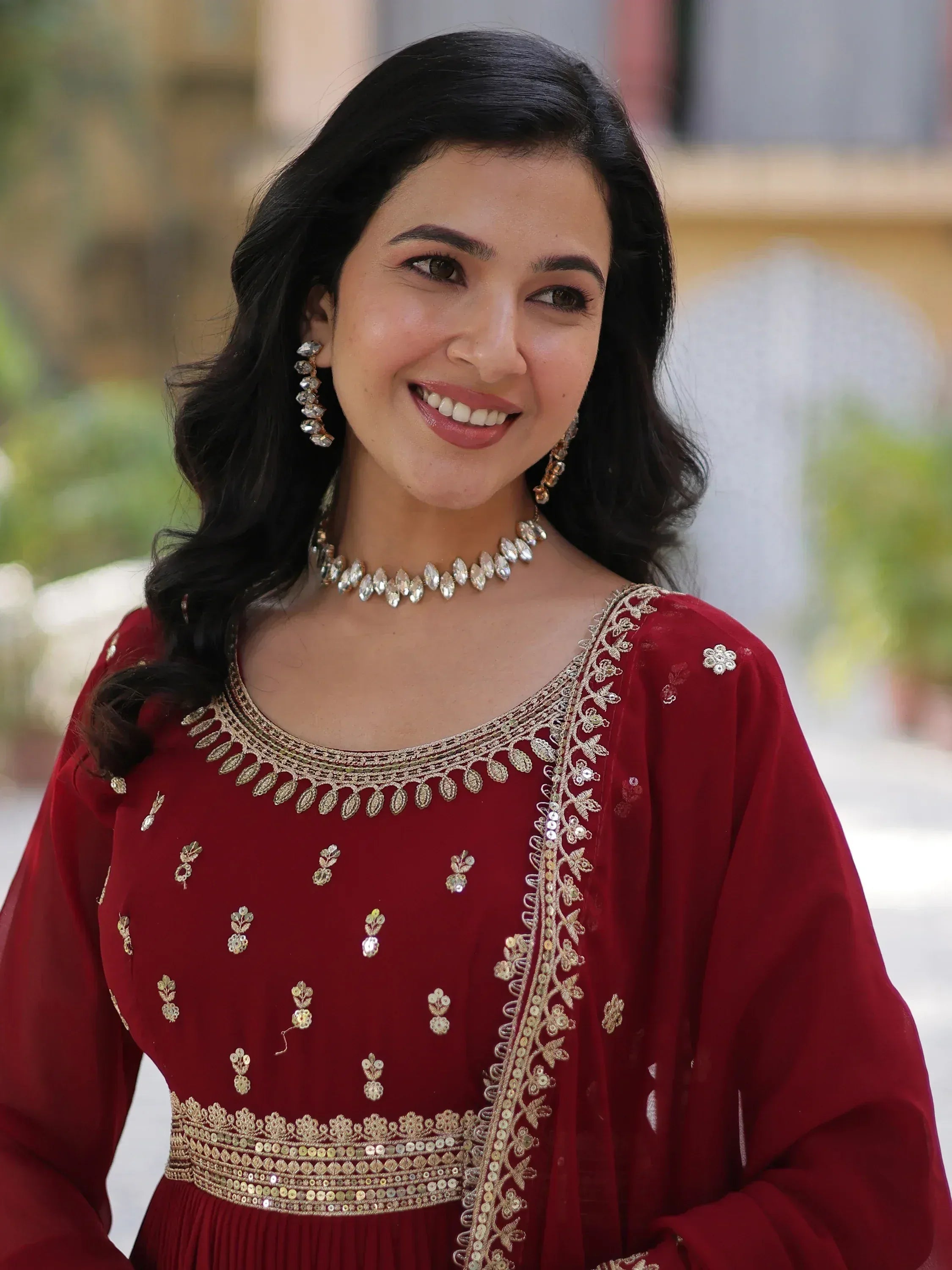 Woman in maroon ethnic gown with gold embroidery and jewelry, perfect for Indian occasions