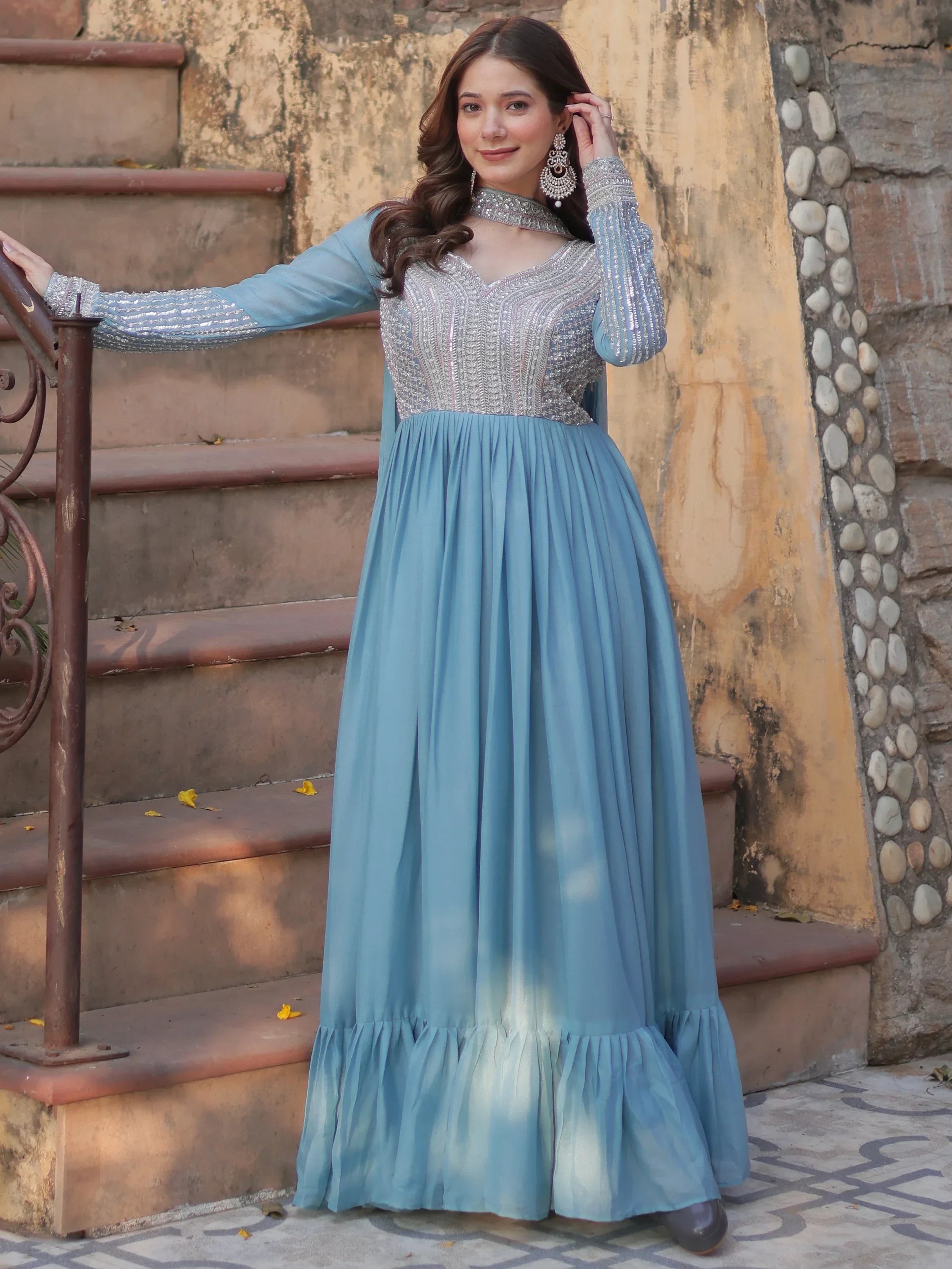 Woman in an embroidered sky blue ethnic gown with long sleeves, standing outdoors
