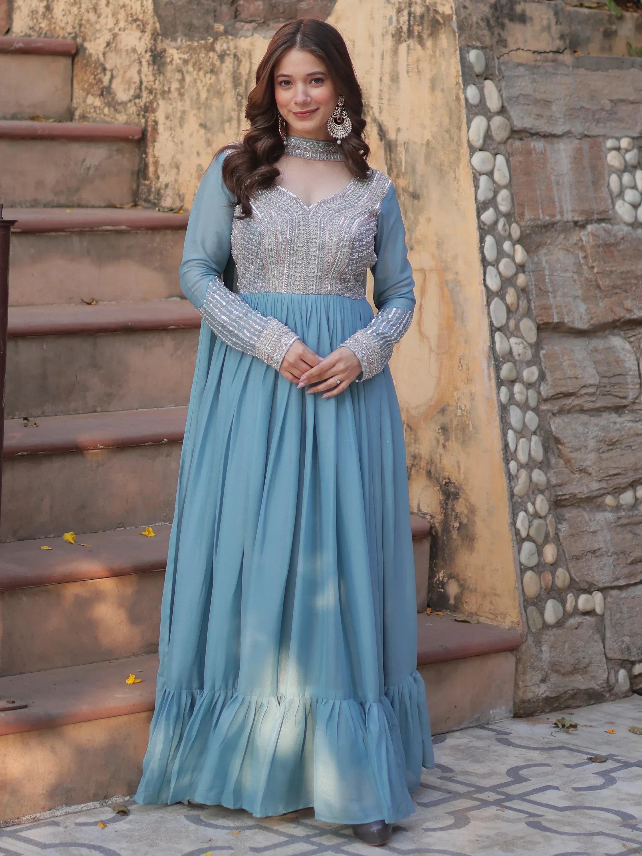 Woman wearing sky blue ethnic gown with silver embroidery, posing outdoors on steps