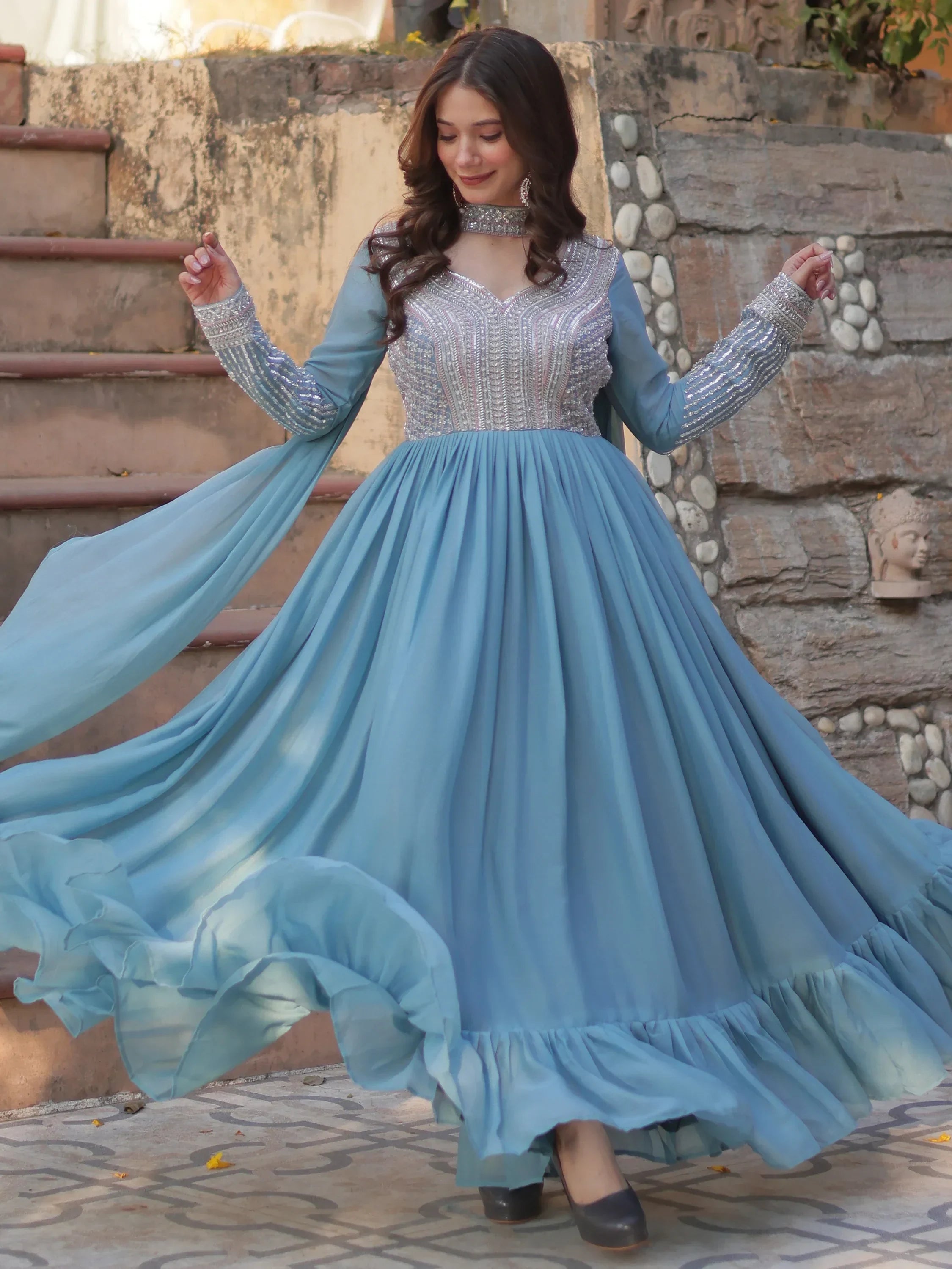 Woman in a sky blue designer Anarkali gown with silver embroidery, posing outdoors.
