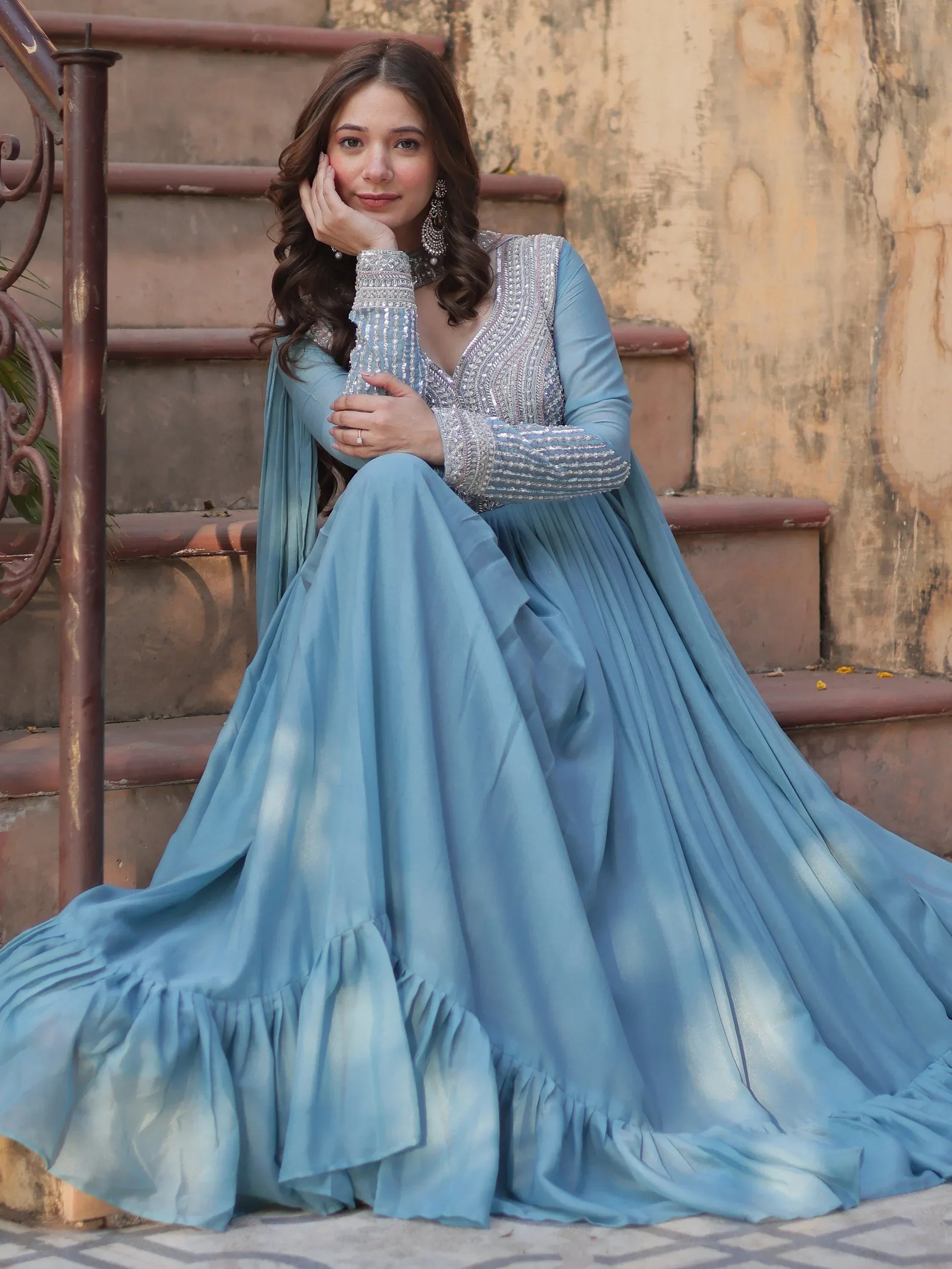 Woman in light blue embellished Indian gown with long sleeves sitting on stairs