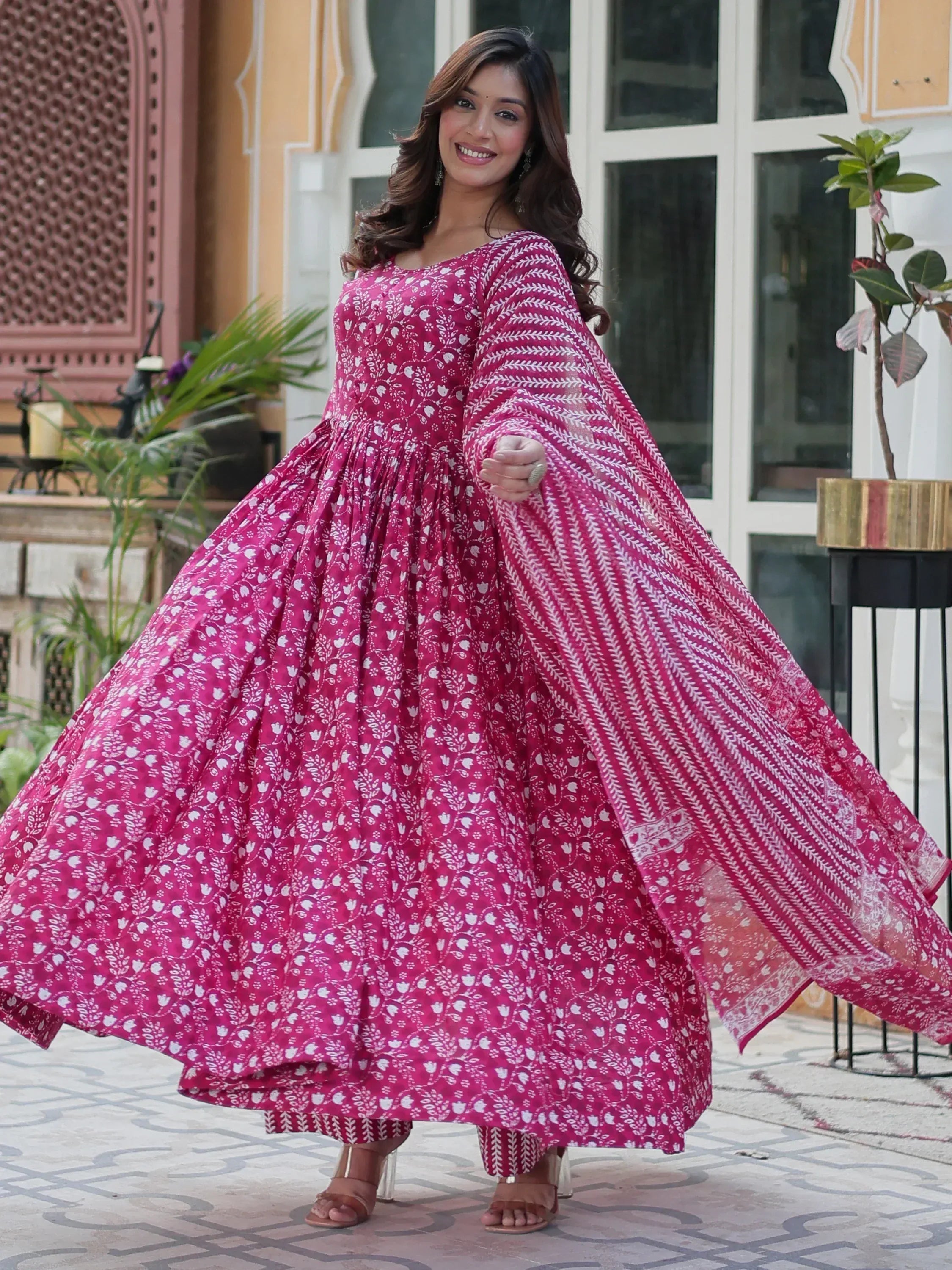 Woman in vibrant pink floral ethnic gown with flowing sleeves, perfect for Indian festive wear.