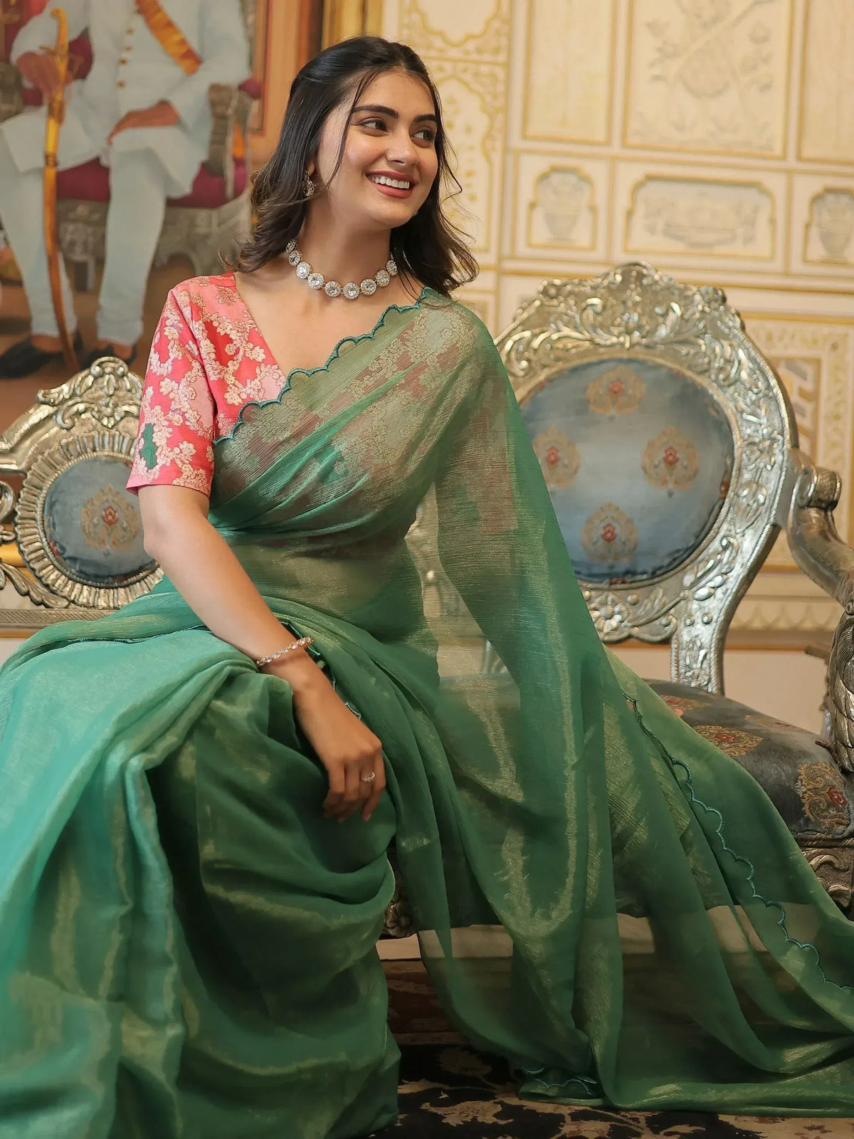 Woman in elegant green saree with pink floral blouse, seated on ornate chair, showcasing Indian ethnic wear