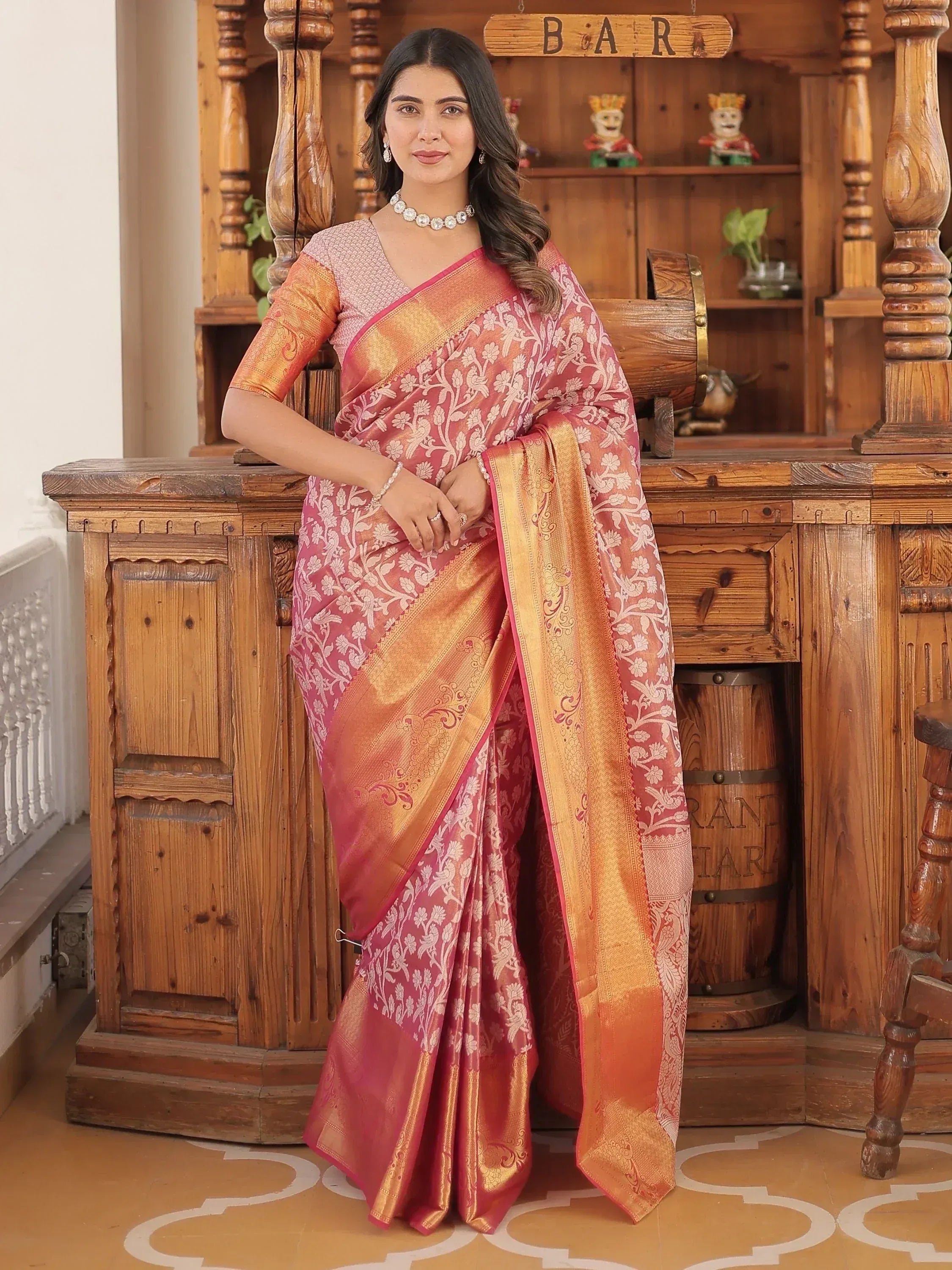 Woman in pink and gold floral designer saree with embroidered border, styled for ethnic occasions