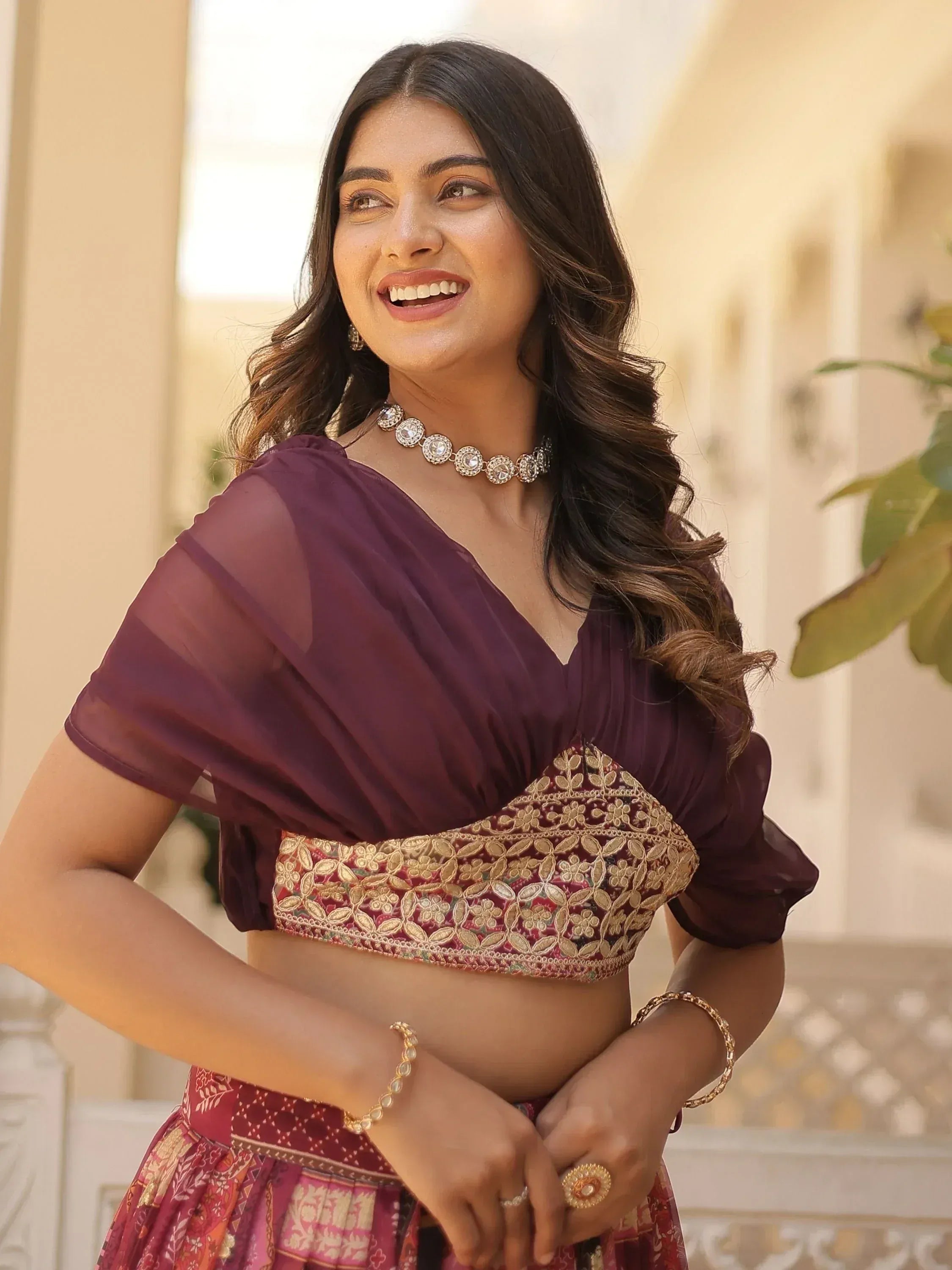 Woman in maroon embroidered lehenga choli with sheer dupatta, gold jewelry, smiling outdoors