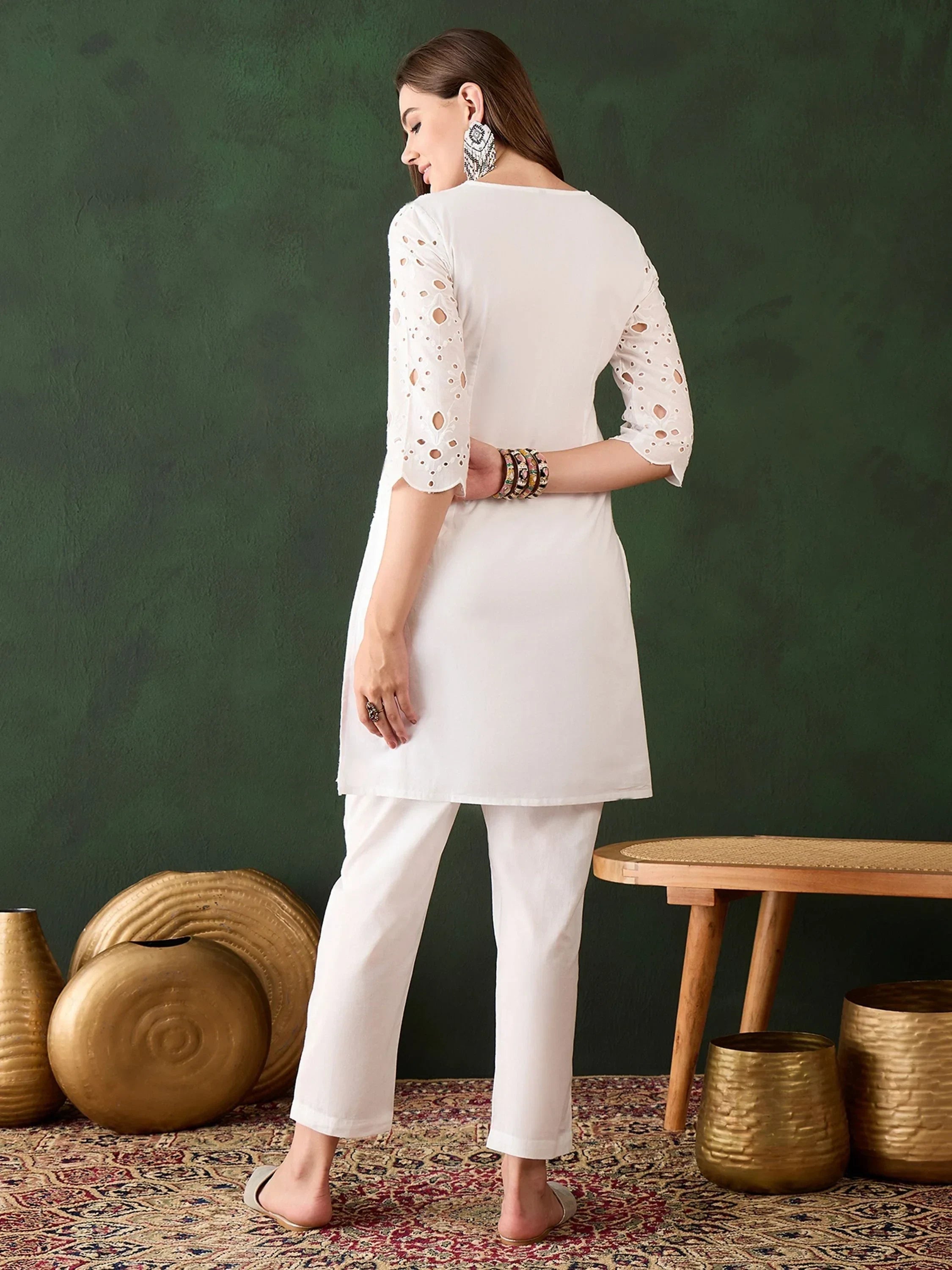 Woman in white kurti and pants with cutwork sleeves, traditional jewelry, standing indoors