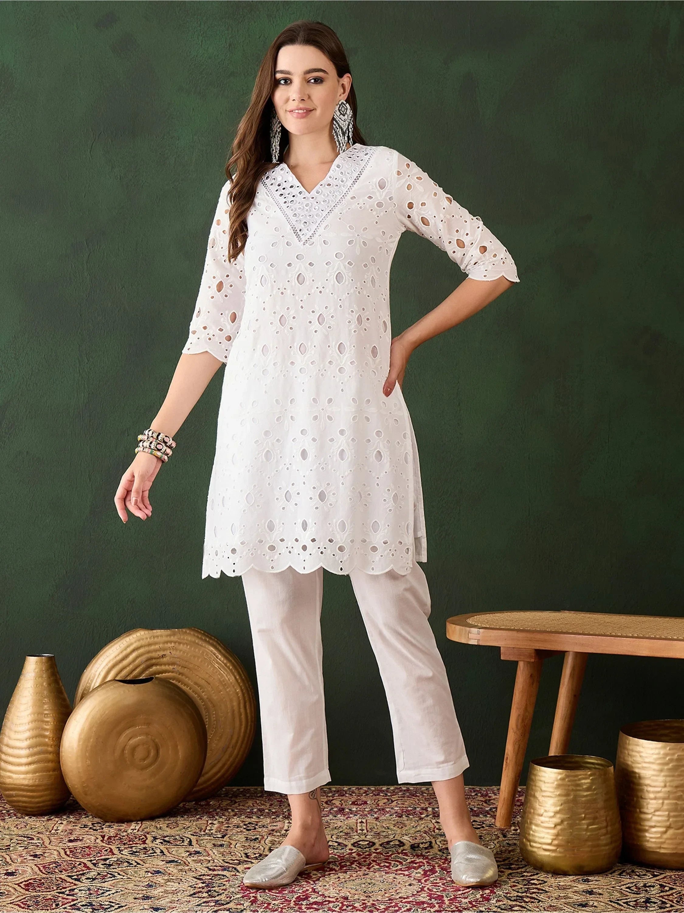 Woman in white embroidered kurti and pants, silver earrings, on patterned rug with gold decor
